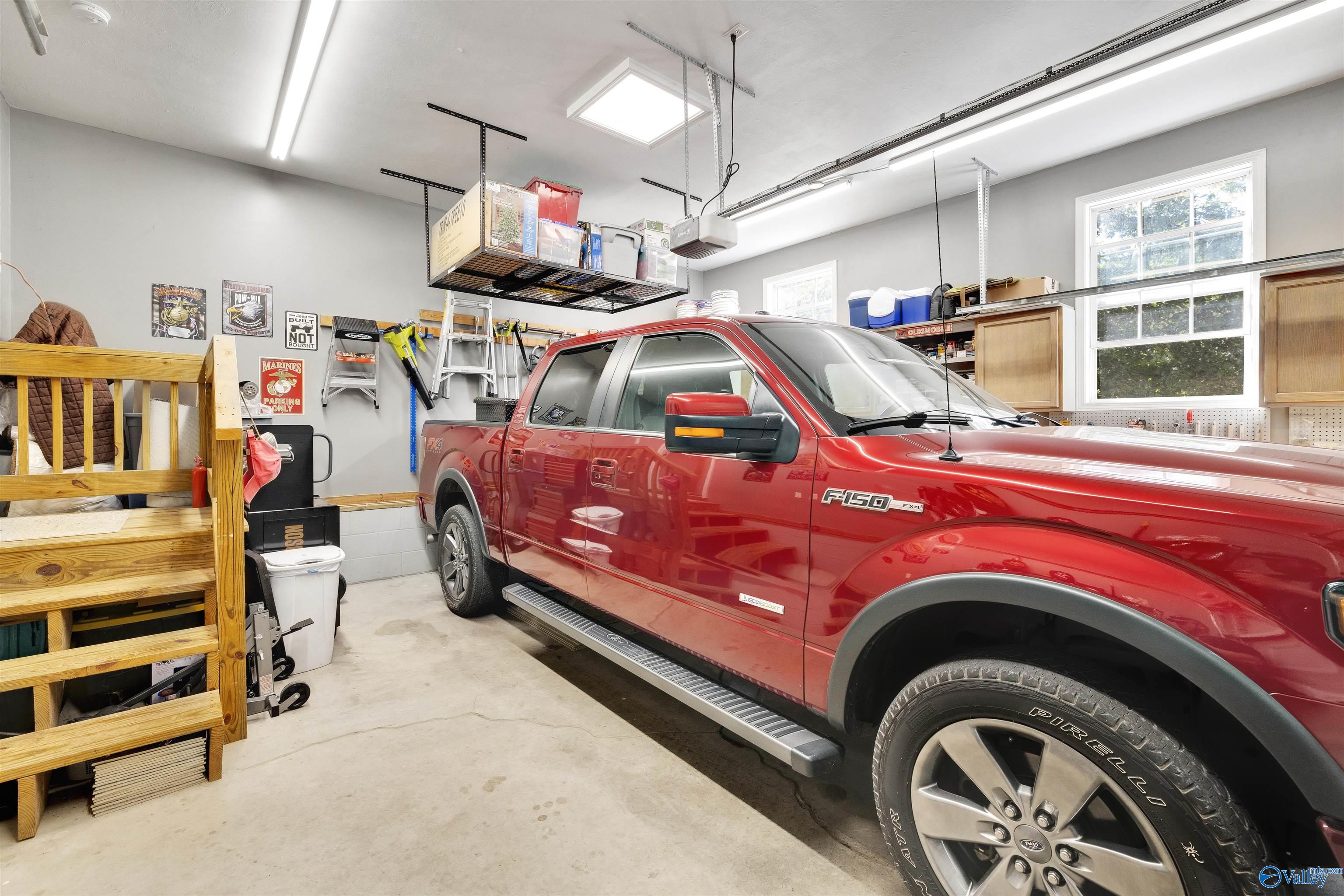 Garage with a red pickup truck, overhead storage racks, and workshop cabinets.