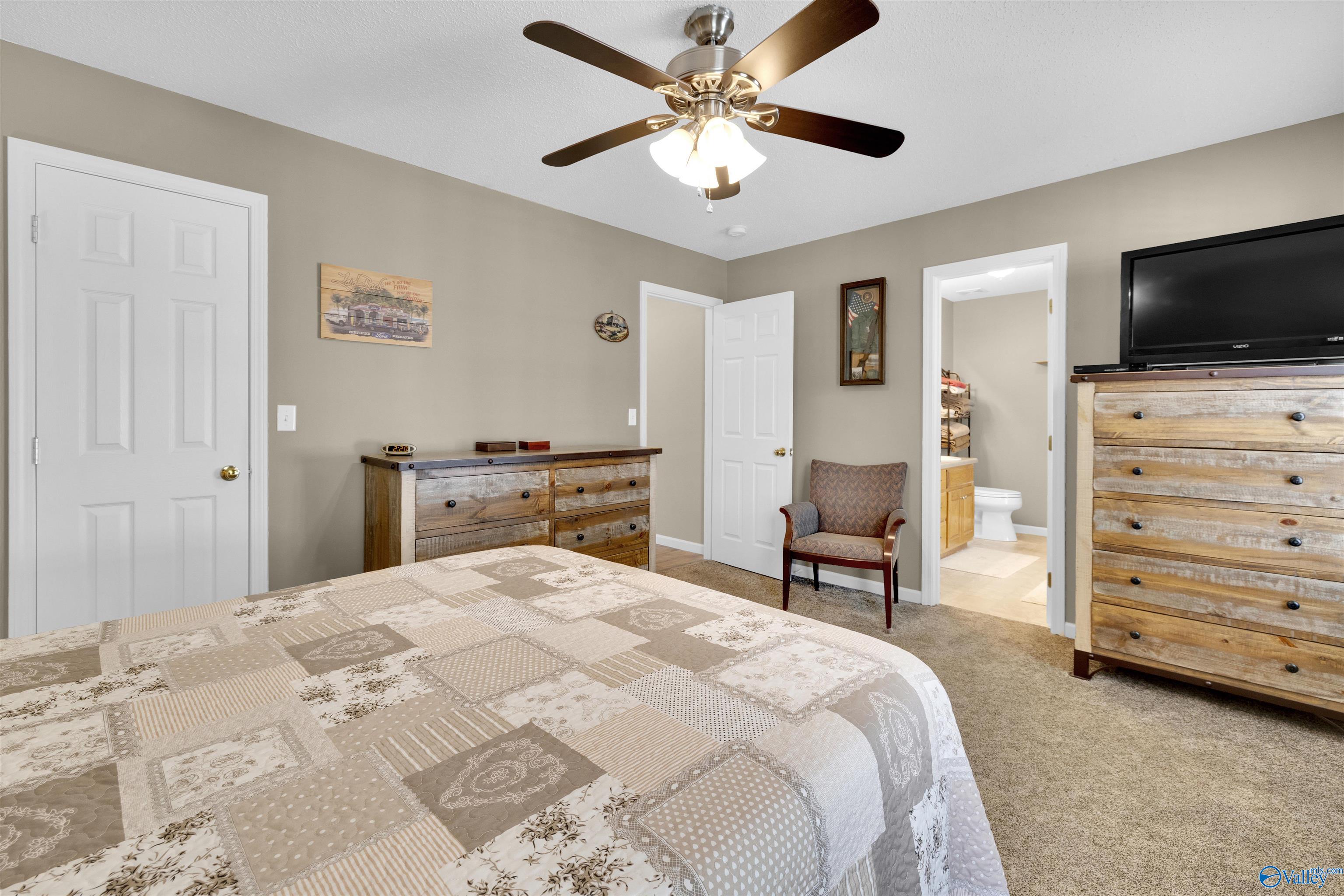 Bedroom with a patchwork quilt, rustic wooden dressers, and an adjoining bathroom visible through the doorway.