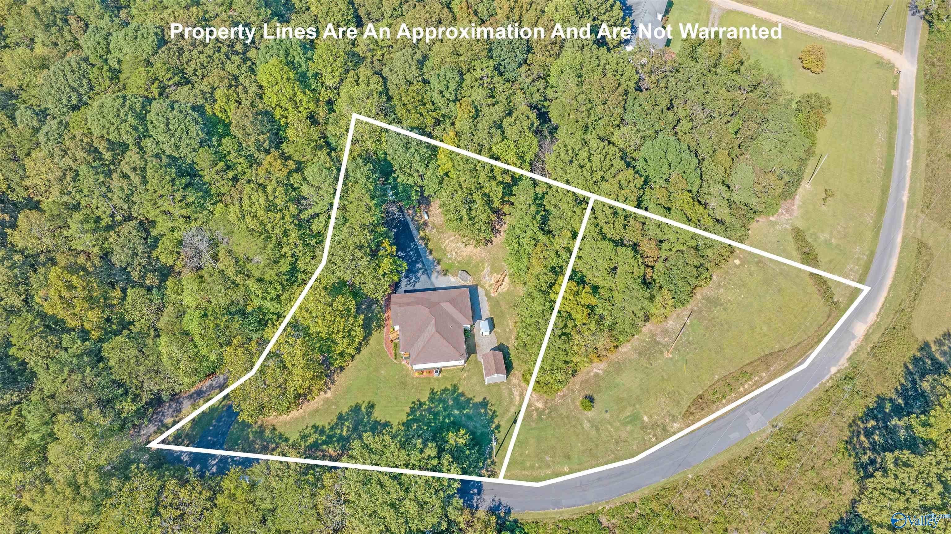 Aerial view of a wooded property with a house, outbuilding, road frontage, and outlined boundaries.