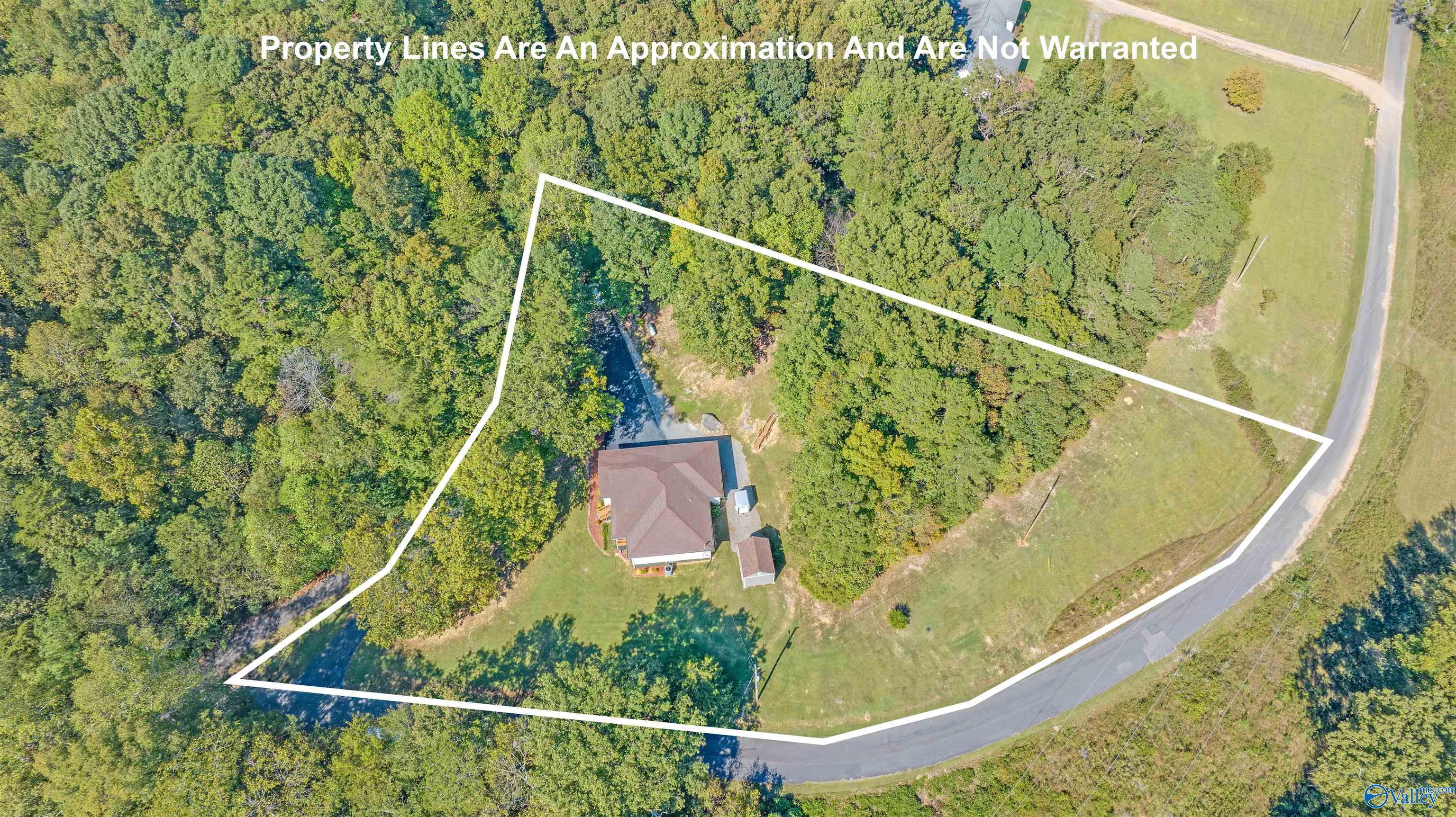Aerial view of a house on a wooded lot outlined by a white property boundary.