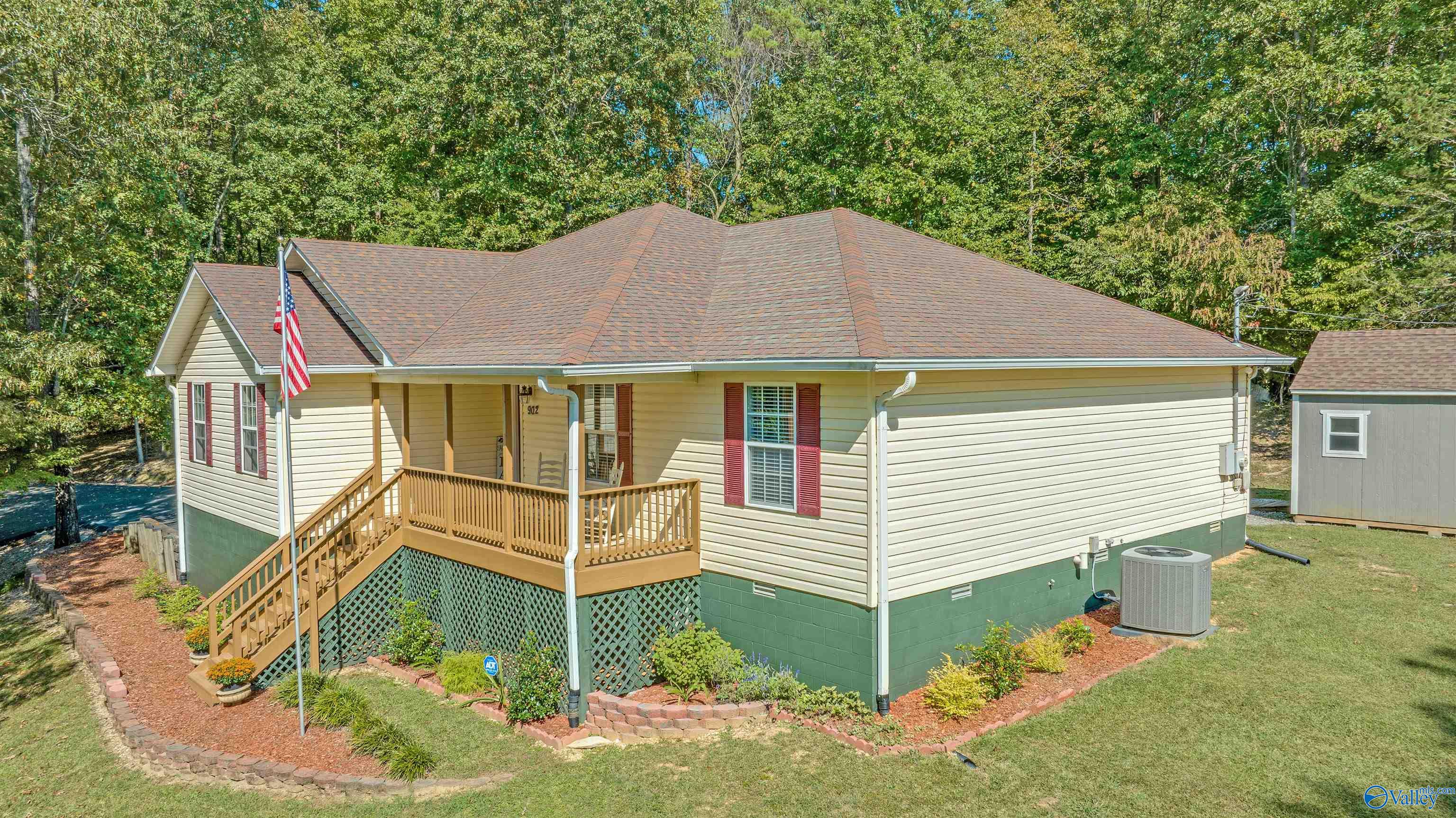 Single-story cream house with a raised wooden porch, American flag, and wooded backdrop.