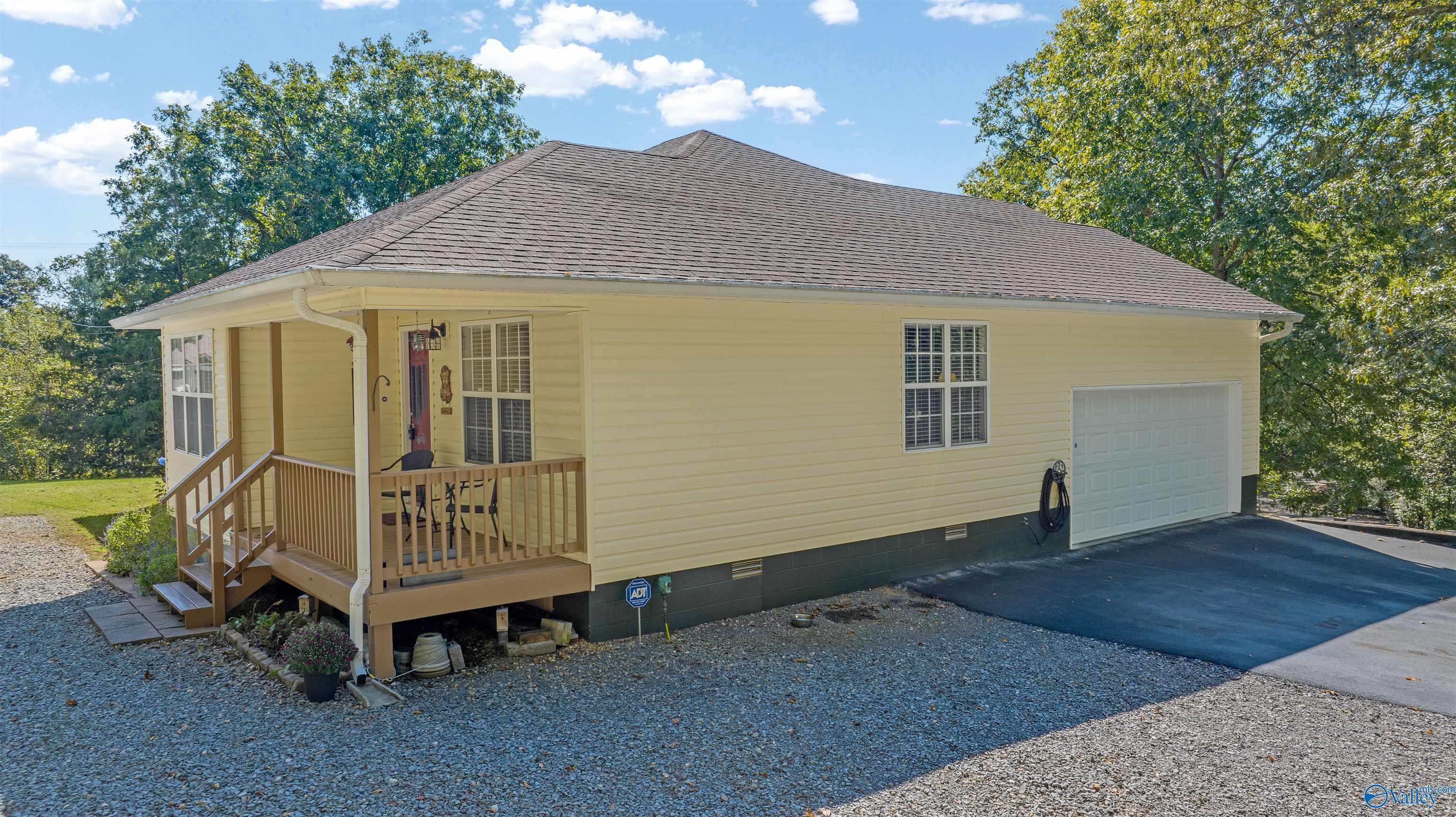 Yellow single-story house with a covered porch, attached garage, and gravel driveway.