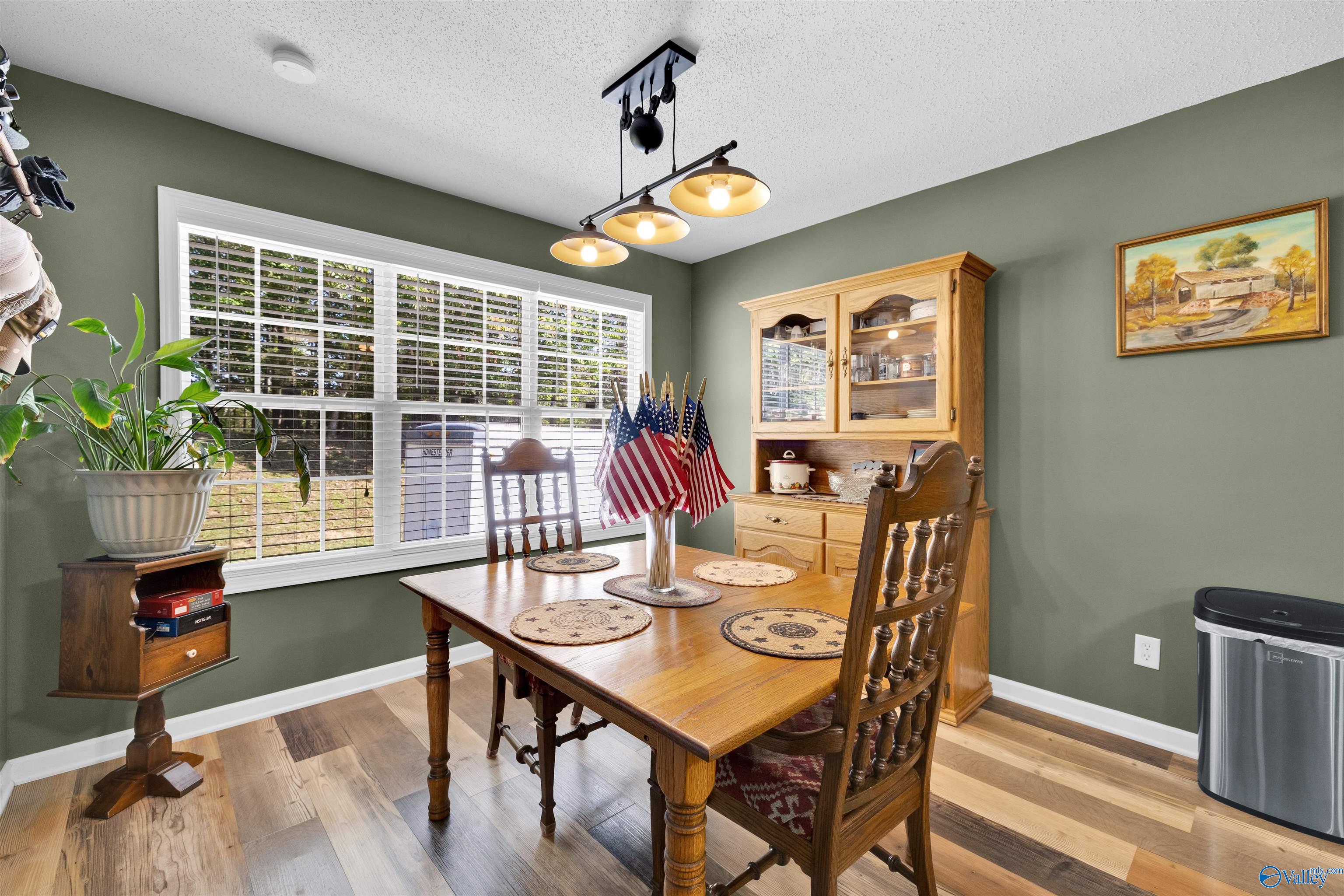 Dining room with a wooden table, matching hutch, green walls, and a large window with white blinds.