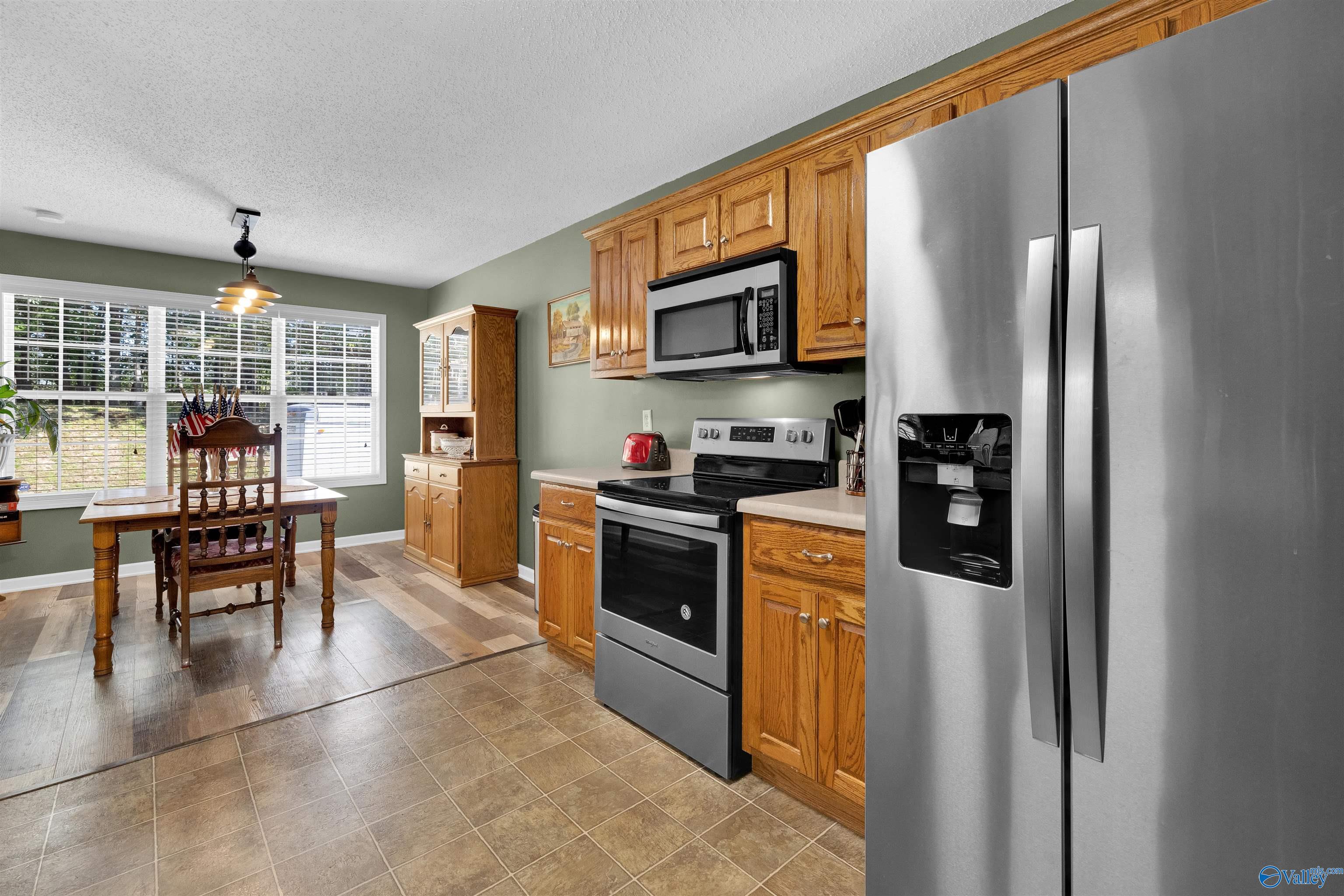 Kitchen with wood cabinets and stainless steel appliances, adjoining a dining area by a large window.