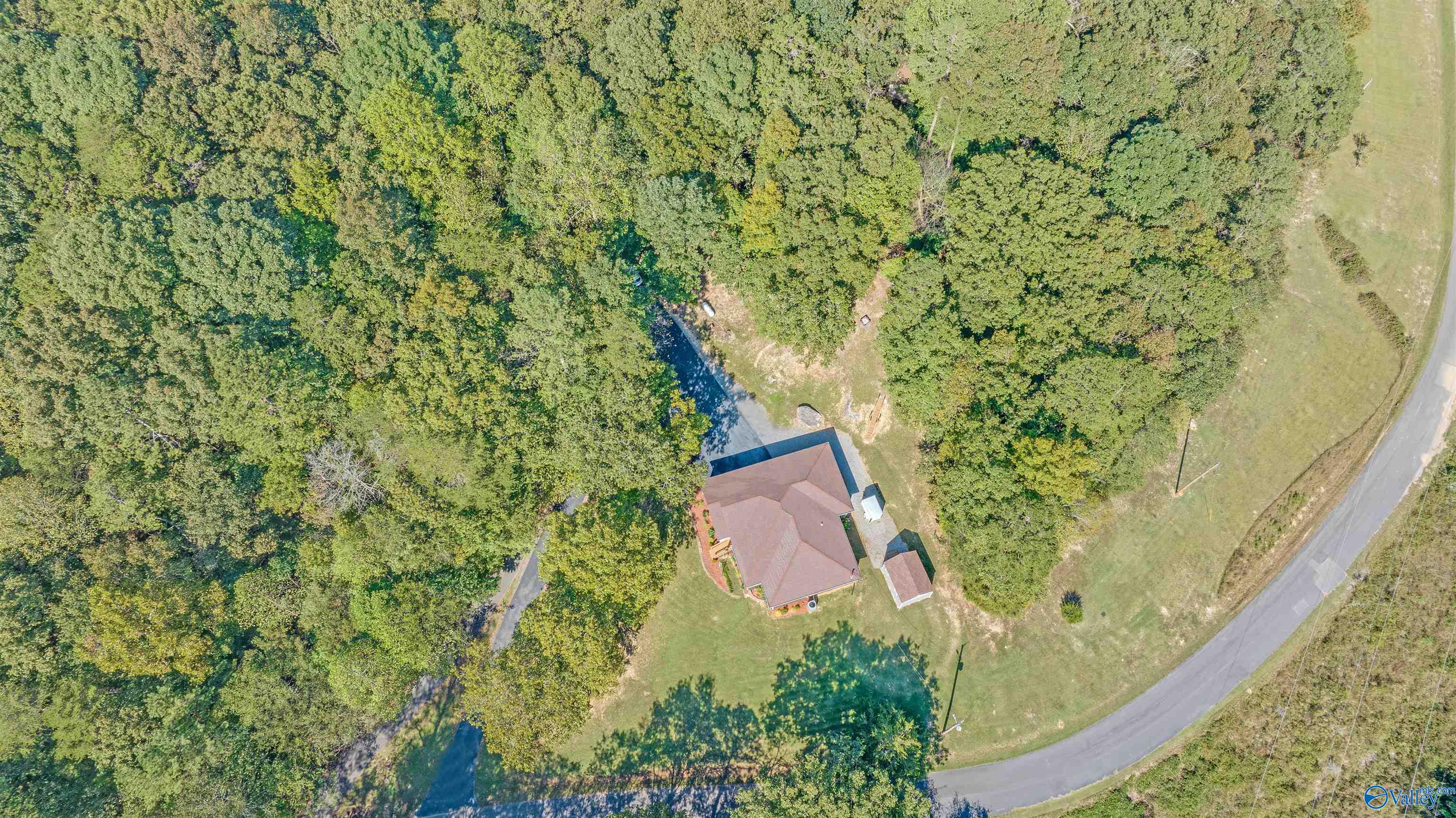 Aerial view of a home on a wooded lot beside a curving road.