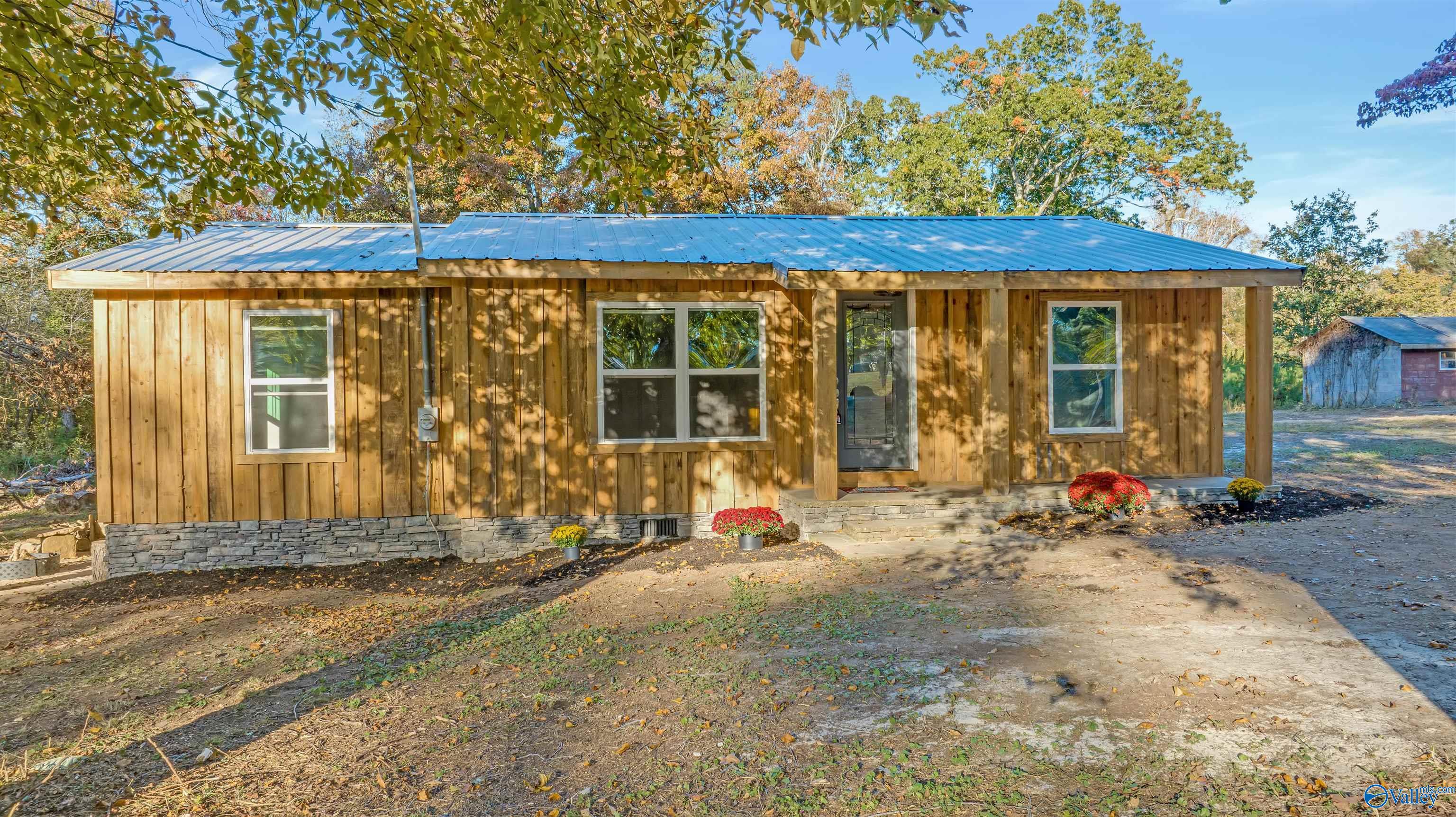 Wood-sided single-story home with a blue metal roof, covered porch, and stone foundation.