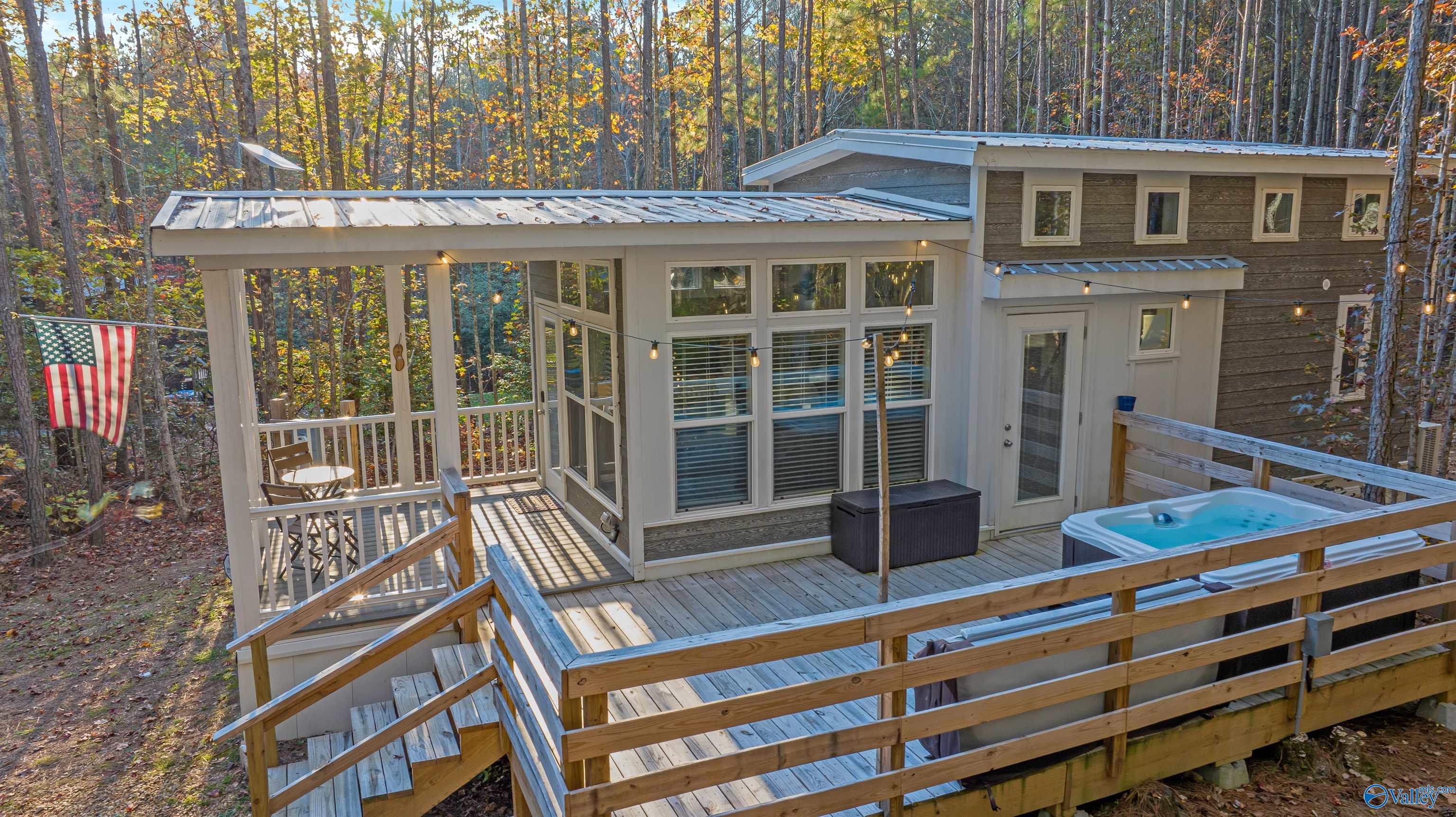 Modern wooded home with a wraparound deck, string lights, and an outdoor hot tub.