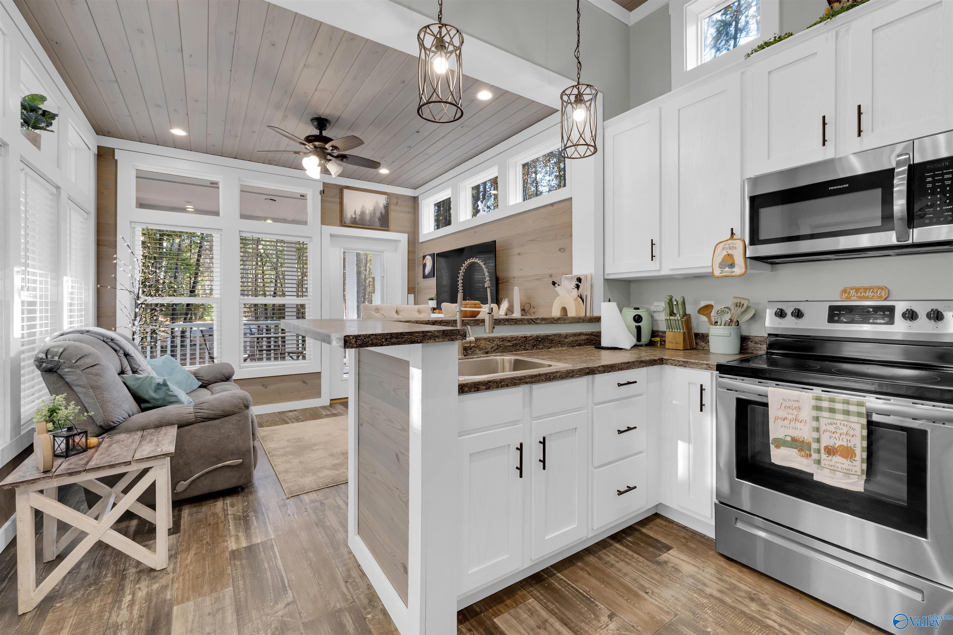 Open-plan kitchen with a large island, white cabinets, stainless appliances, and an adjoining living area with a gray recliner.