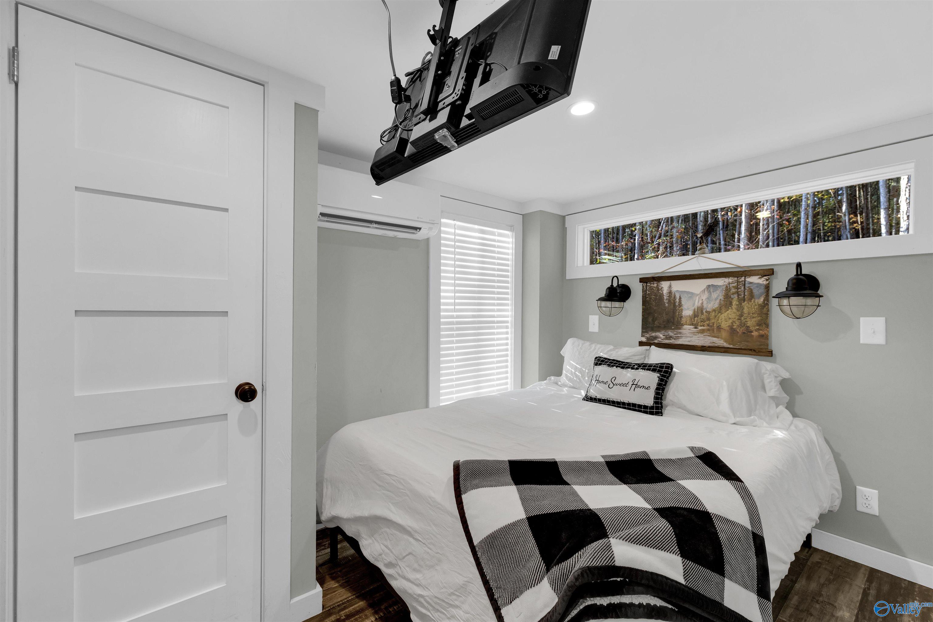 Staged bedroom with a white bed, checkered throw, and high window overlooking trees.