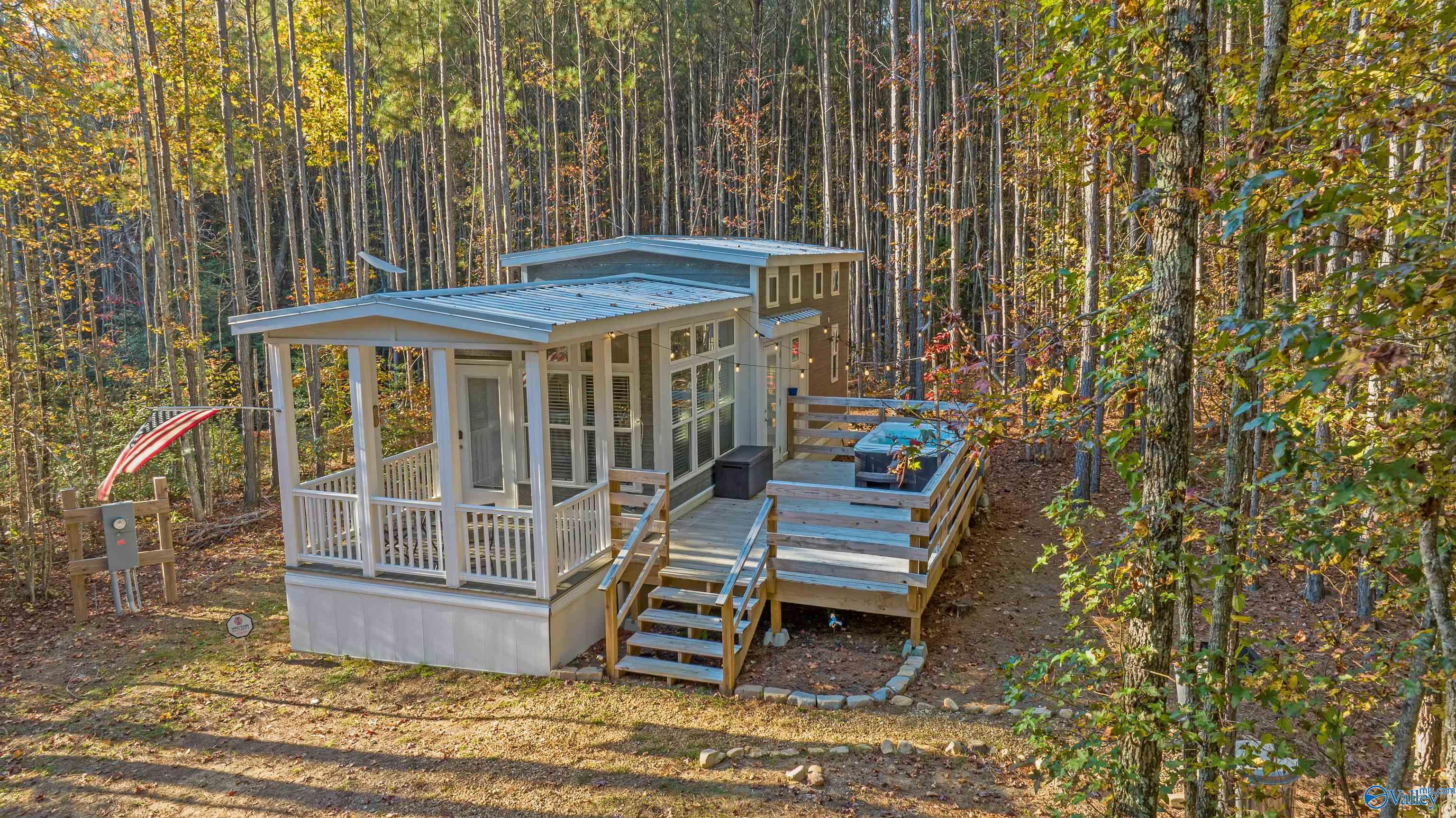 Modern cabin in autumn woods with a covered porch, raised deck, and hot tub.