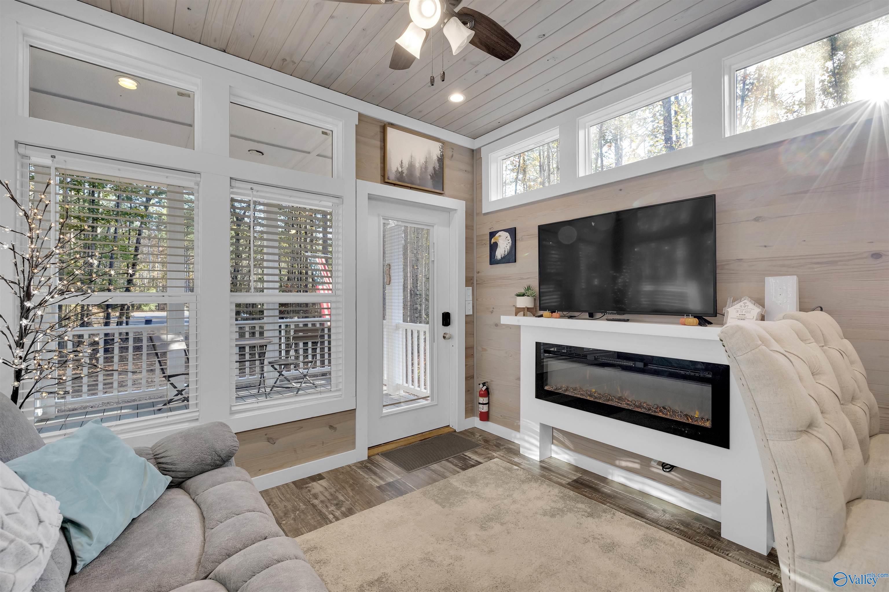 Living room with a TV above a modern fireplace, high plank ceiling, and large windows overlooking trees.