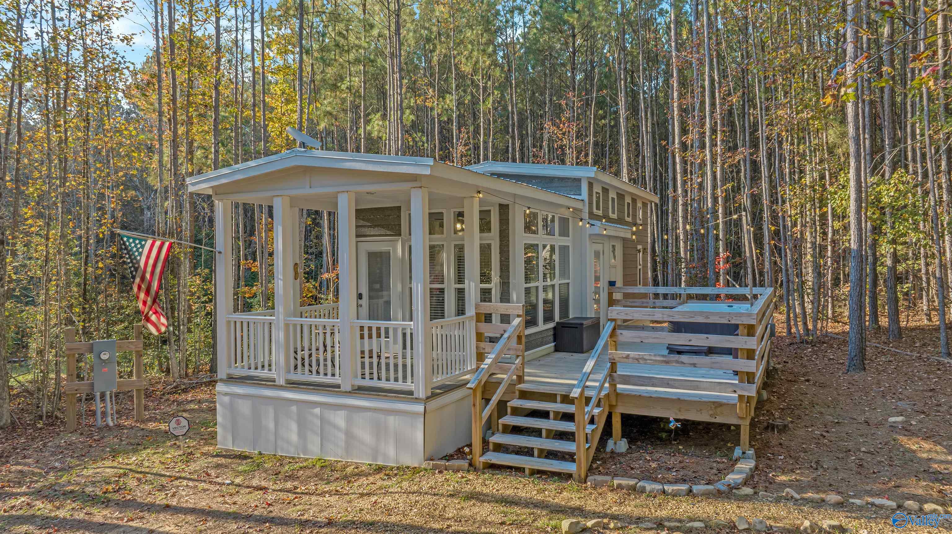 Modern home with a covered porch and raised deck among autumn trees, with an American flag by the porch.