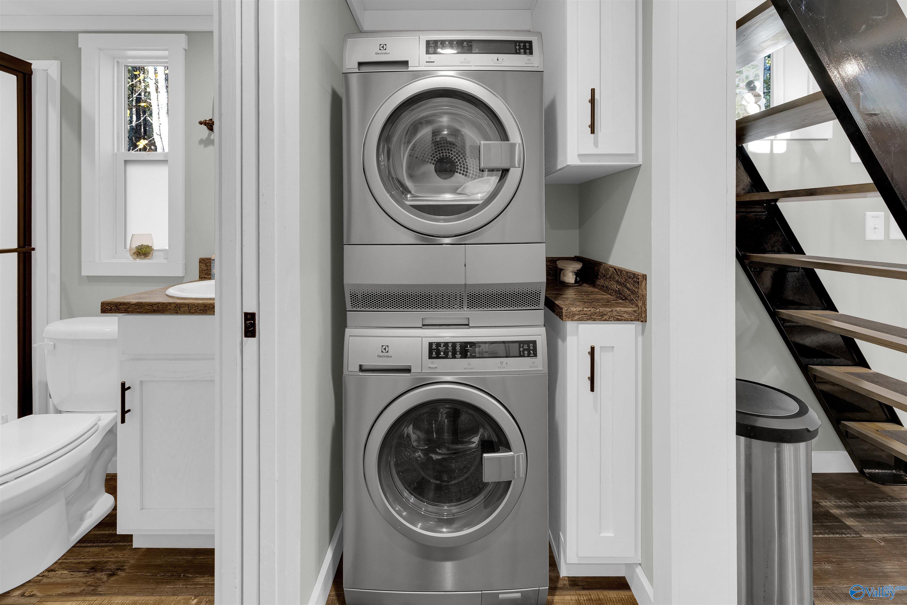 Stacked washer and dryer in a compact laundry area beside a bathroom and open staircase.