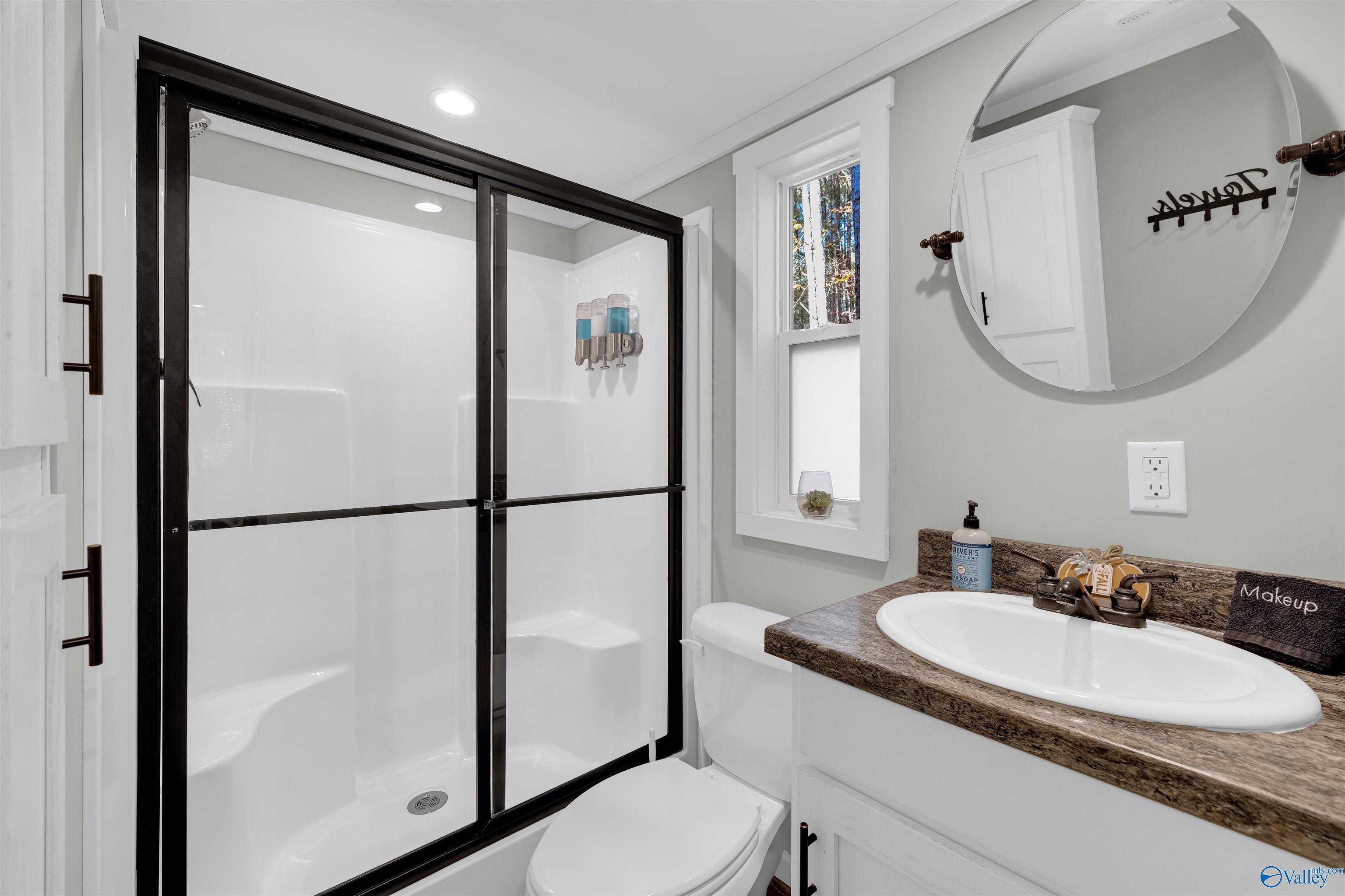 Bathroom with black-framed glass shower doors, a toilet, and a white vanity with a stone countertop.