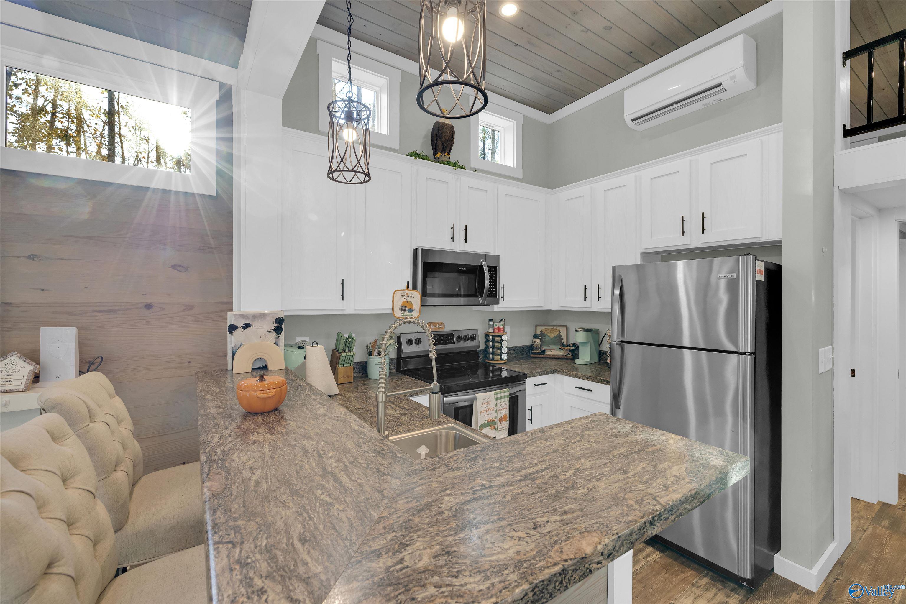 Kitchen with a large stone island, white cabinets, stainless steel appliances, and high windows.