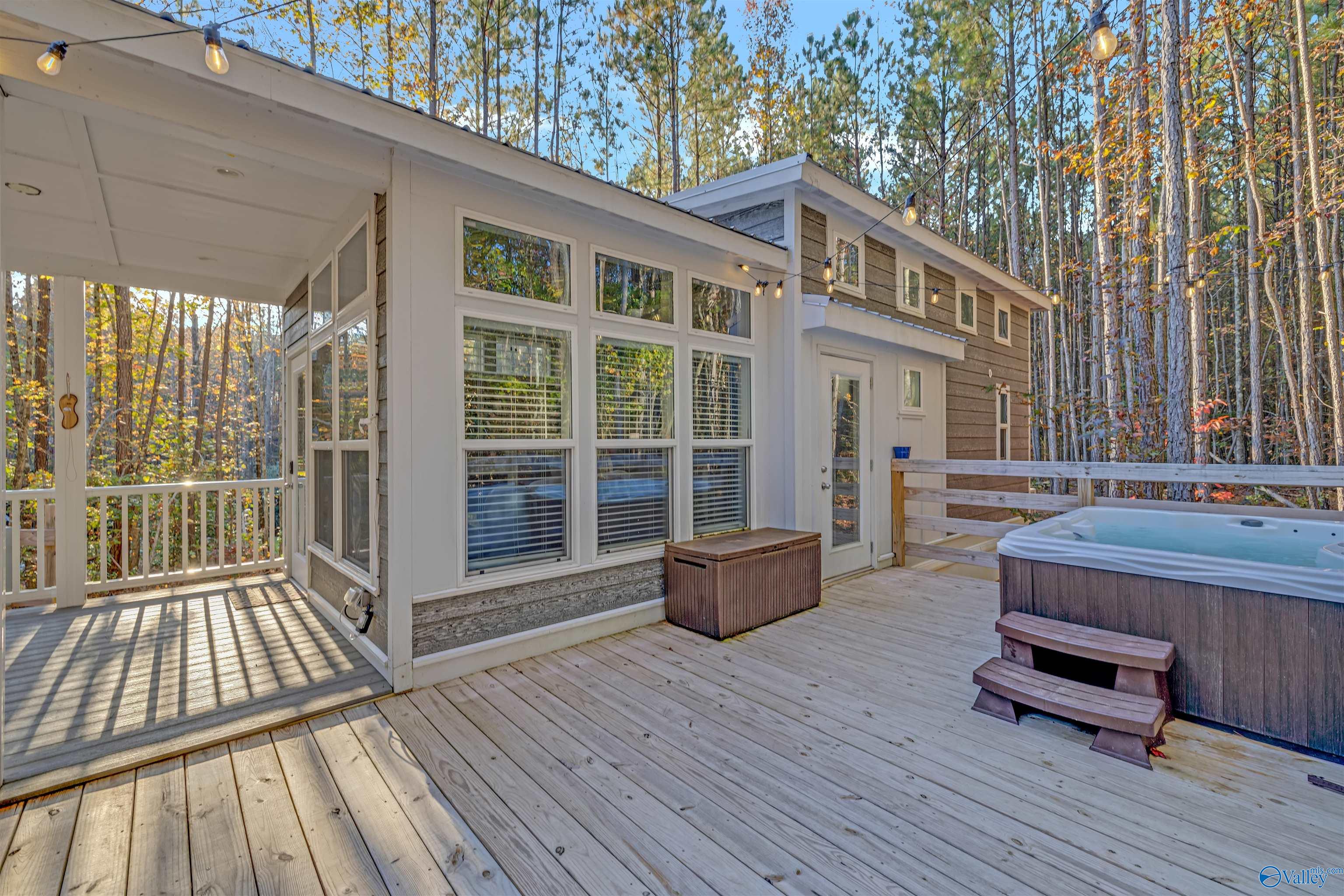 Modern house deck with a covered porch, string lights, and a hot tub among autumn trees.