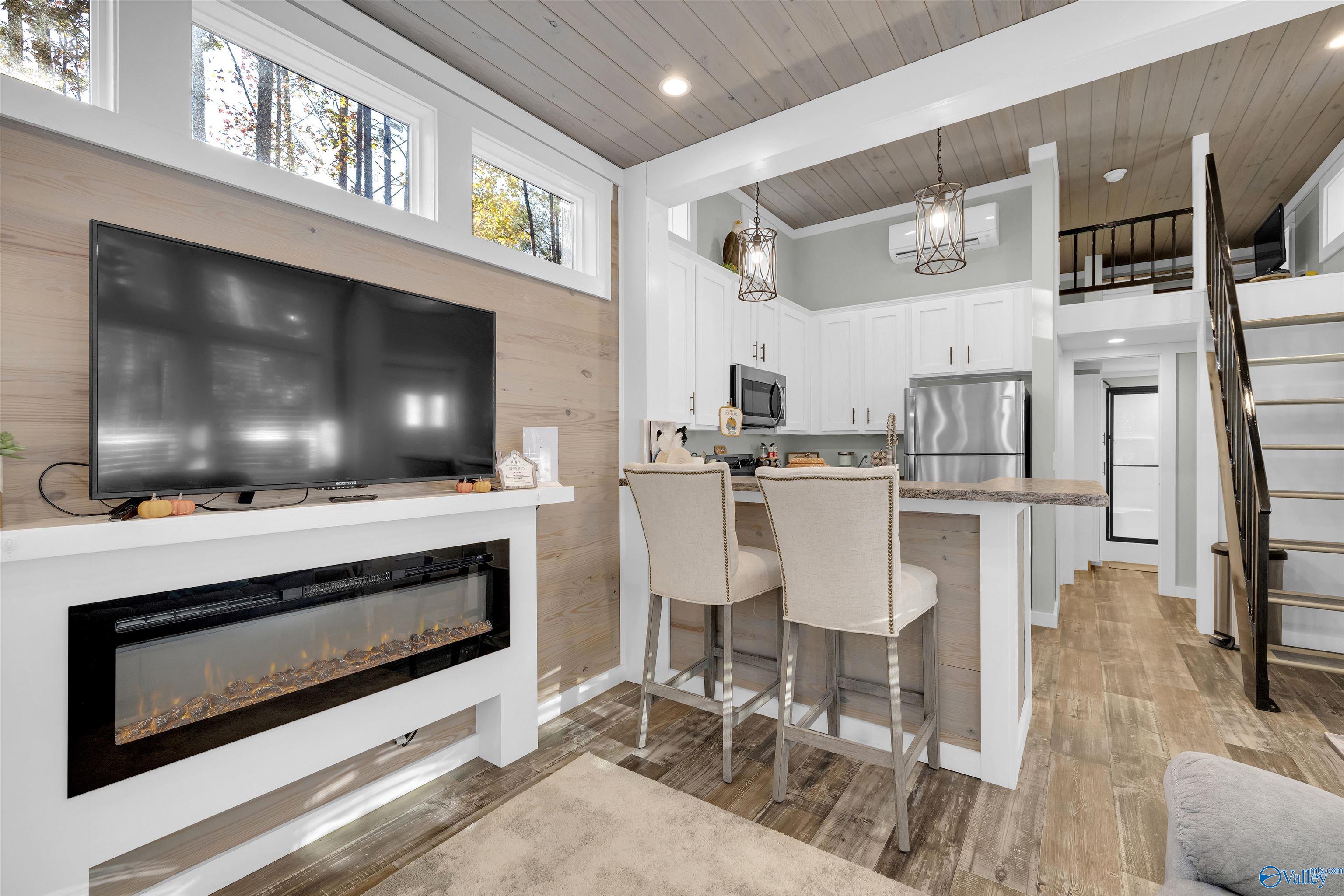 Open-plan living room and kitchen with a fireplace, breakfast bar, vaulted wood ceiling, and loft stairs.