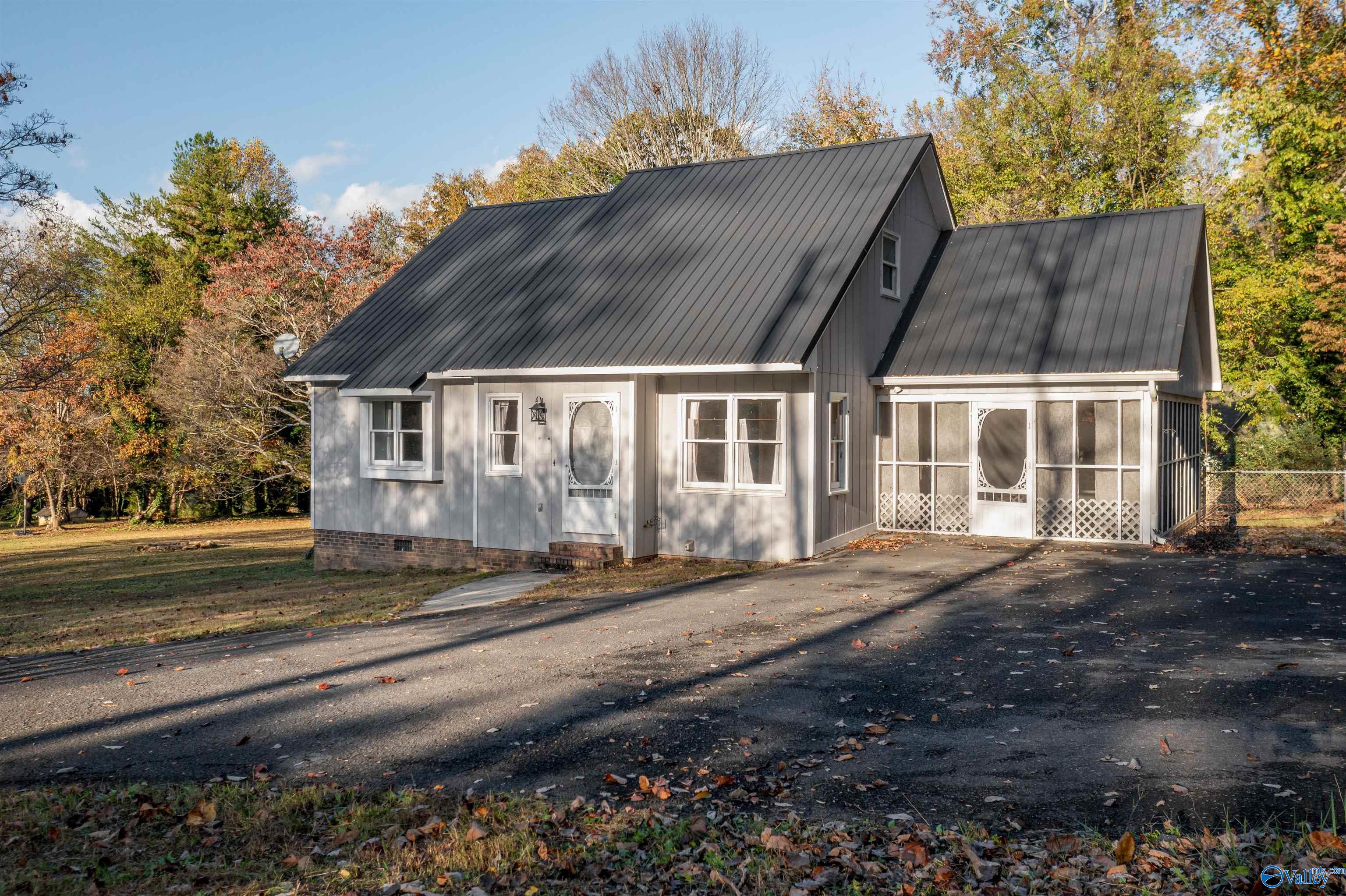 Gray house with a steep metal roof and screened porch, surrounded by autumn trees.