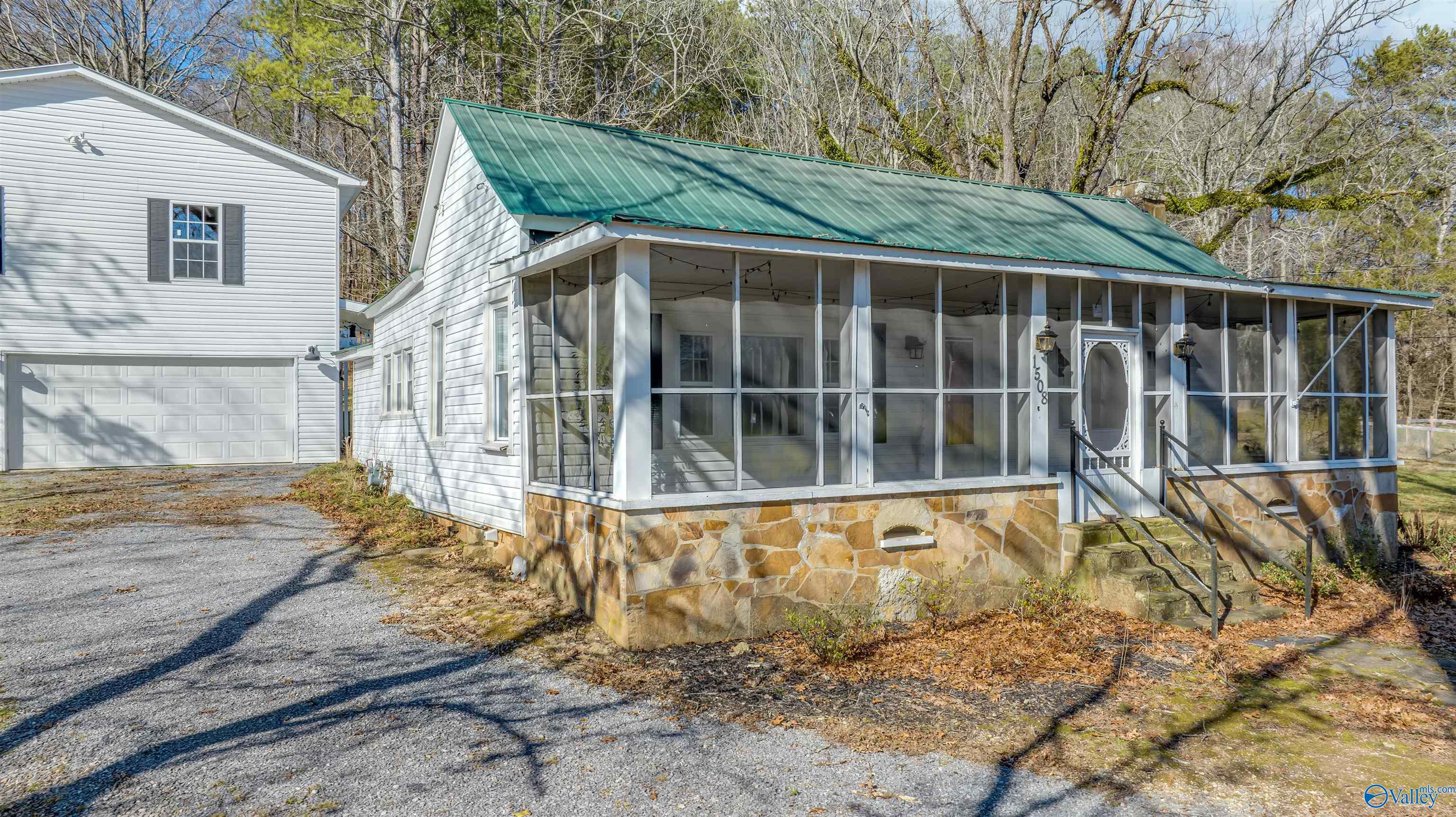 White house with a green metal roof, screened porch, stone foundation, and attached garage.