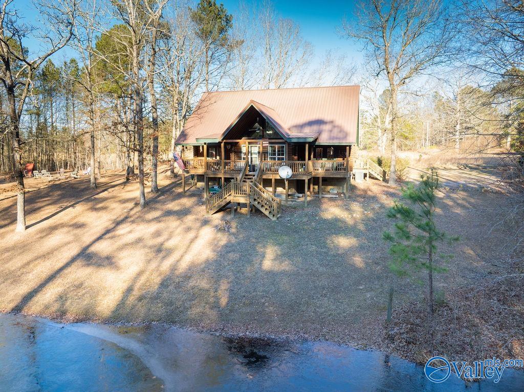 Wooden cabin with a raised porch among bare trees beside a pond.
