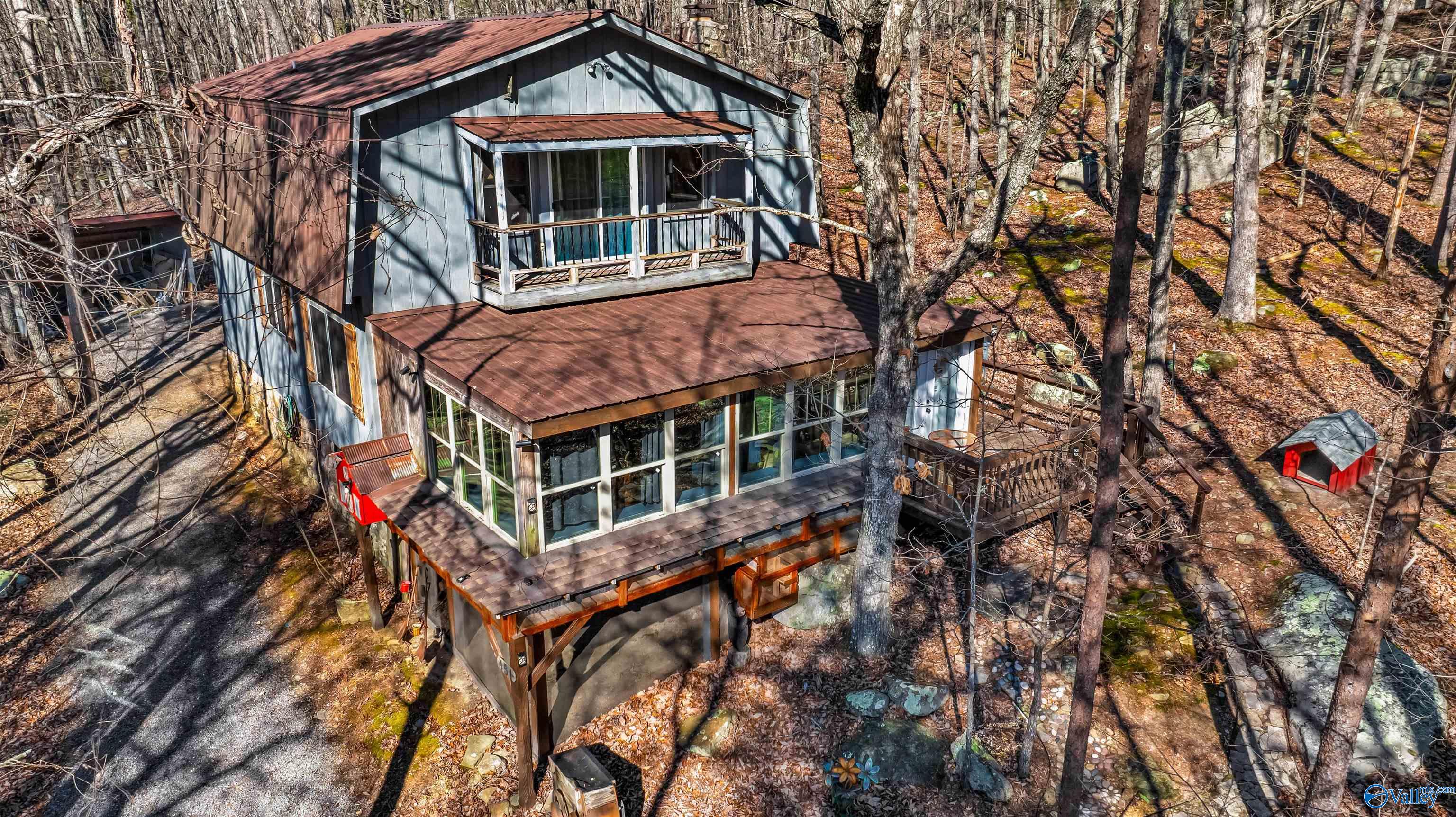 Two-story cabin with large windows and decks nestled among leafless trees.