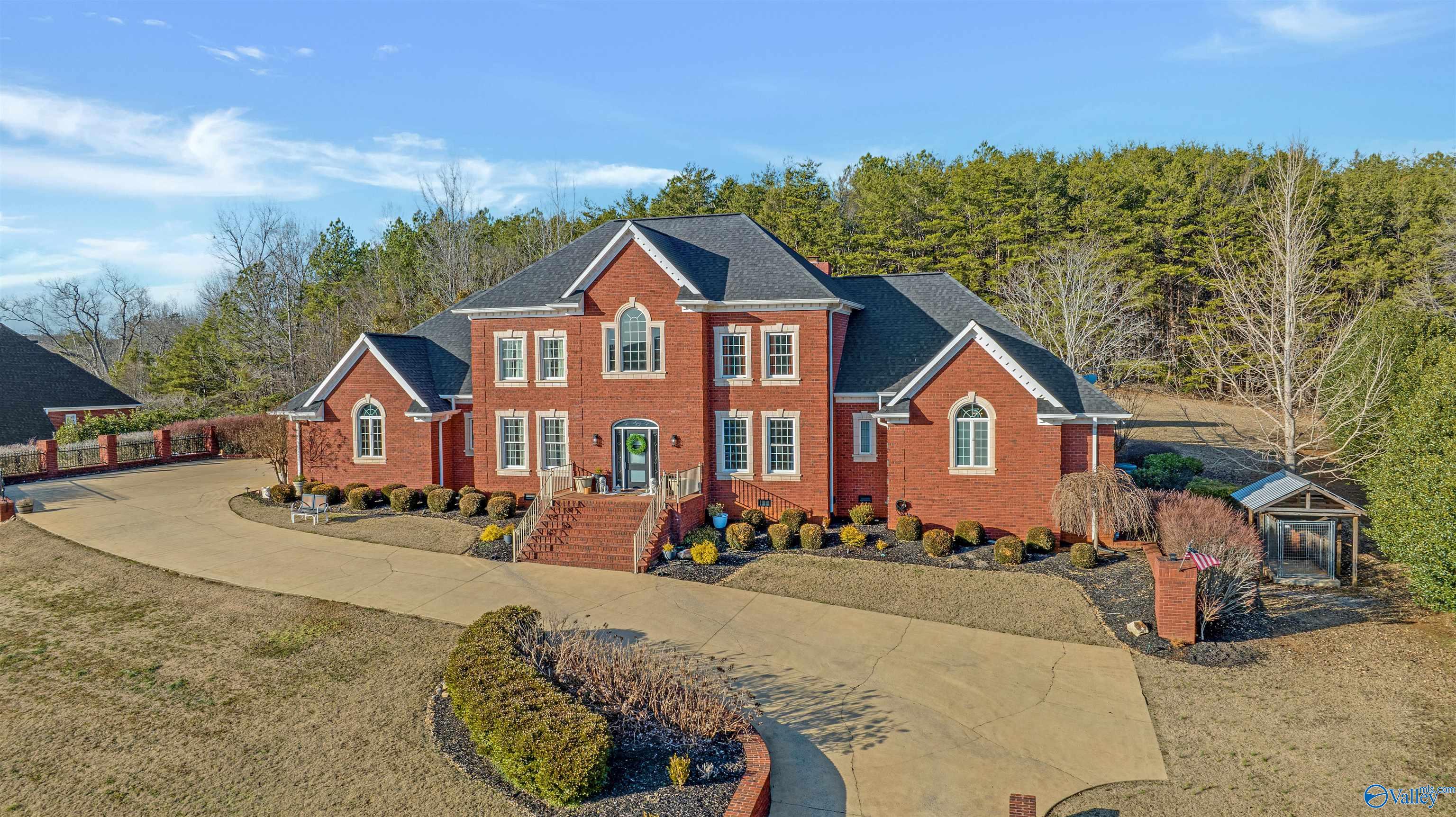 Two-story red brick house with a curved driveway and wooded backdrop.