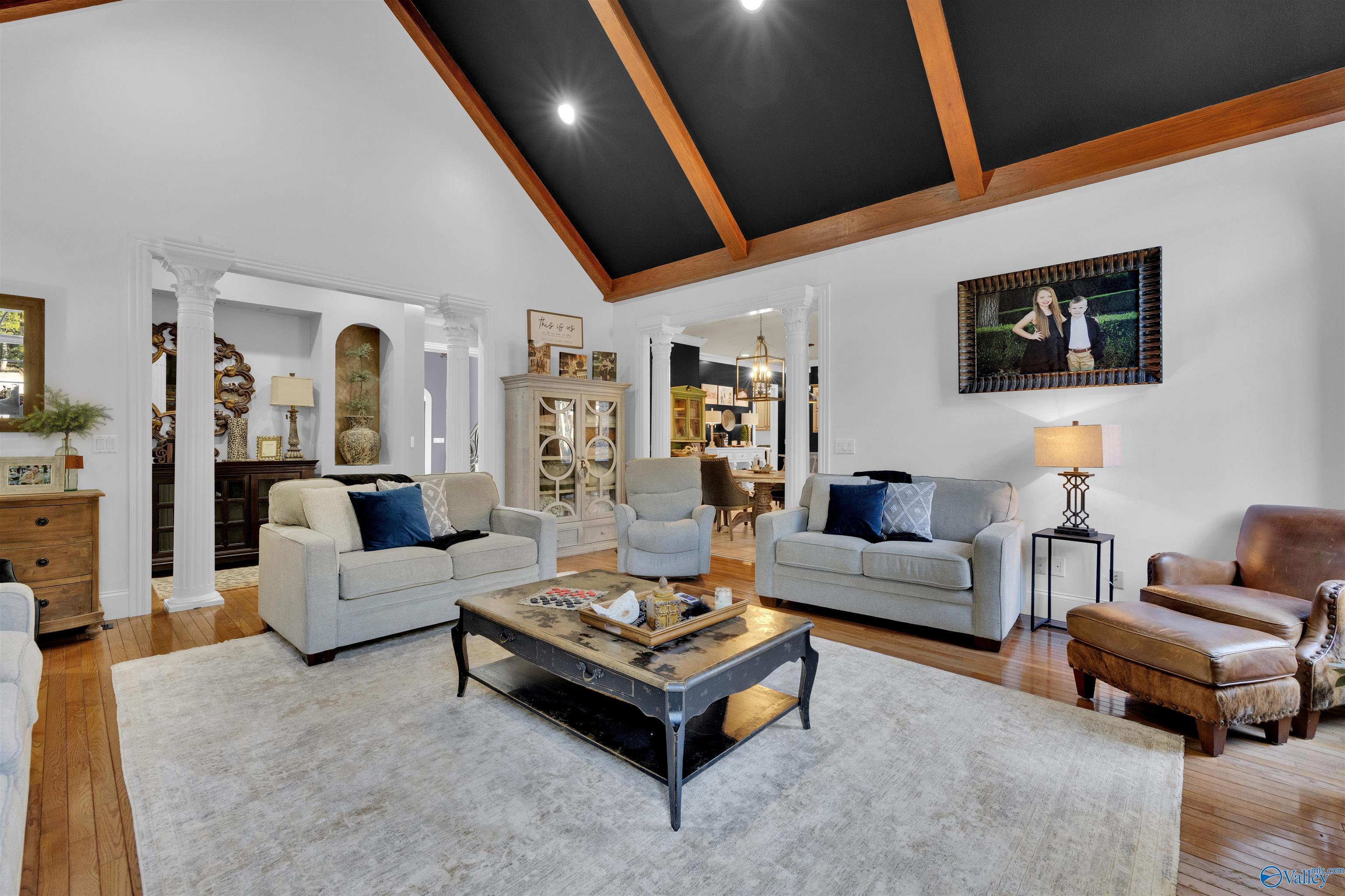 Living room with exposed wood ceiling beams, gray sofas, white columns, and a leather armchair.