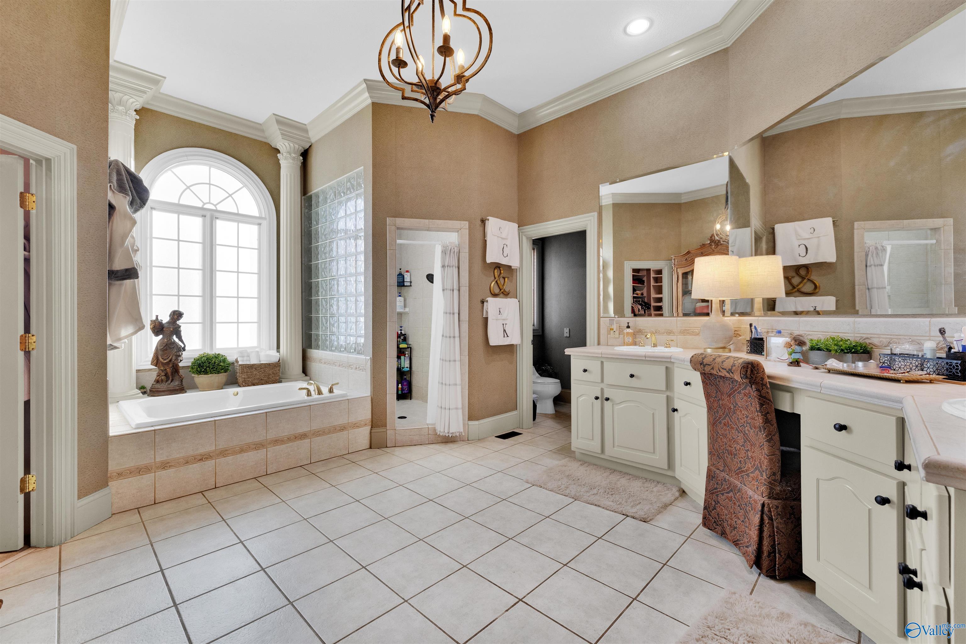 Spacious bathroom with a soaking tub beneath an arched window and a long double vanity.