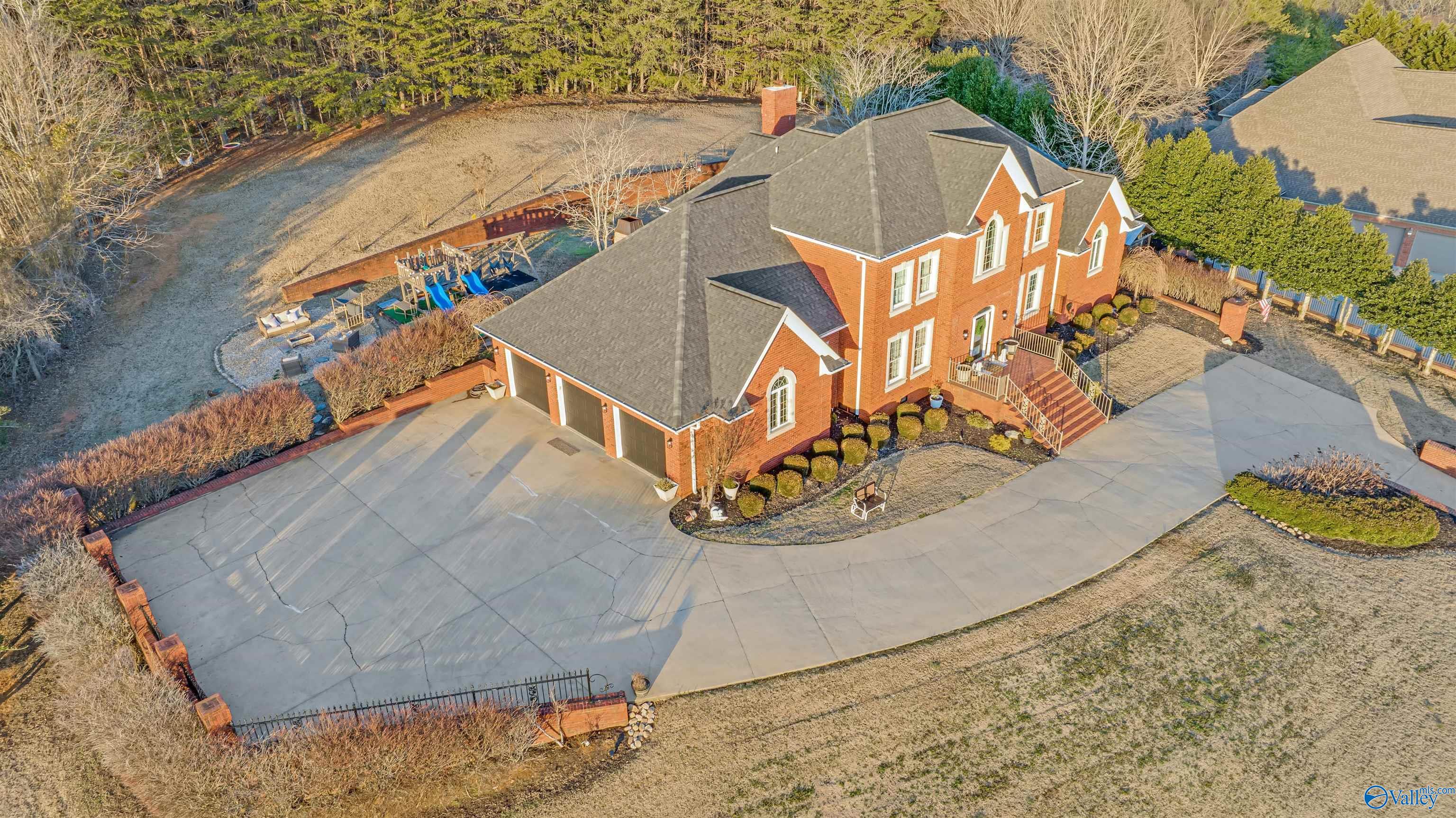 Aerial view of a red brick two-story home with a circular driveway and backyard playset.