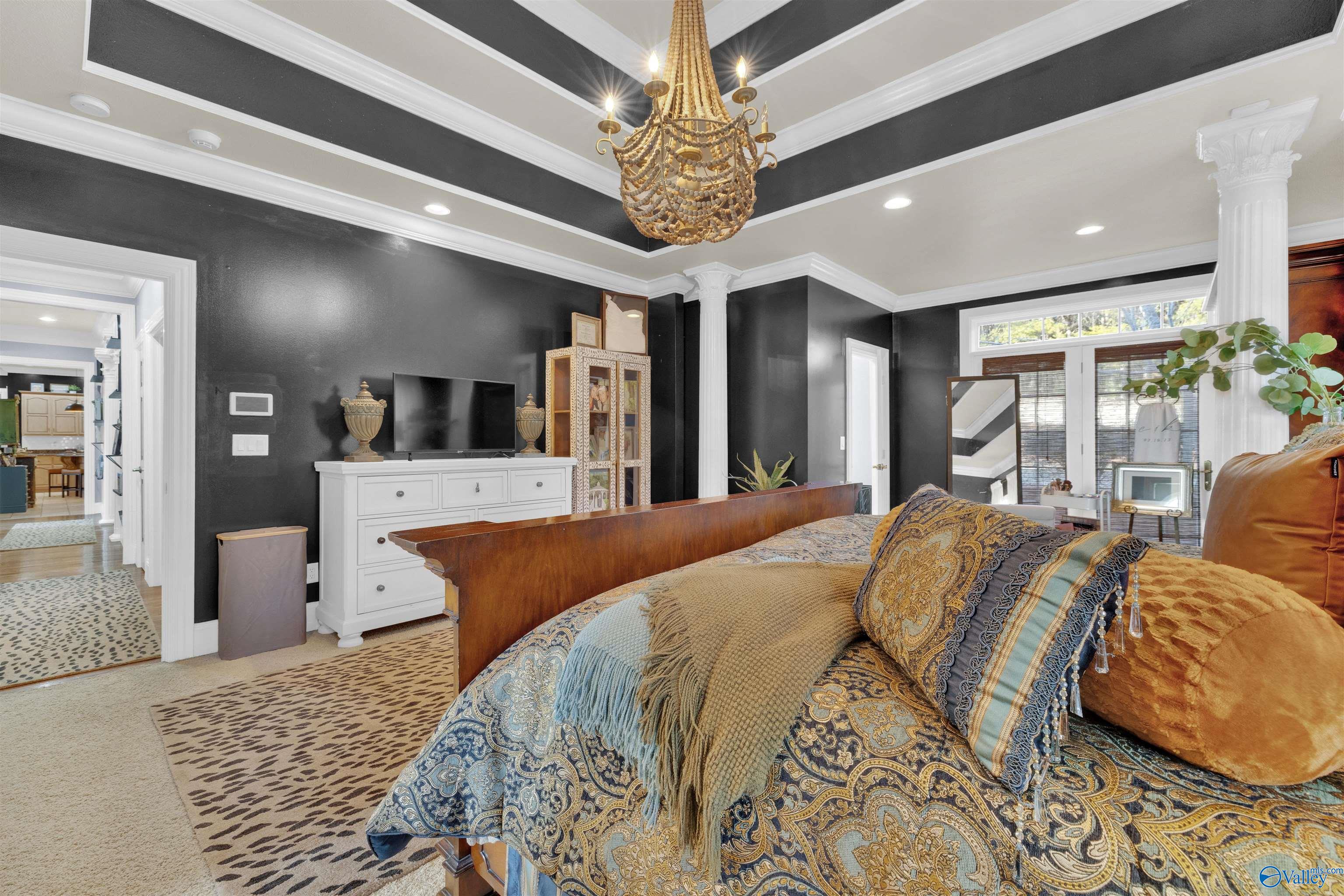 Bedroom with ornate blue-and-gold bedding, dark walls, white columns, and a beaded chandelier.