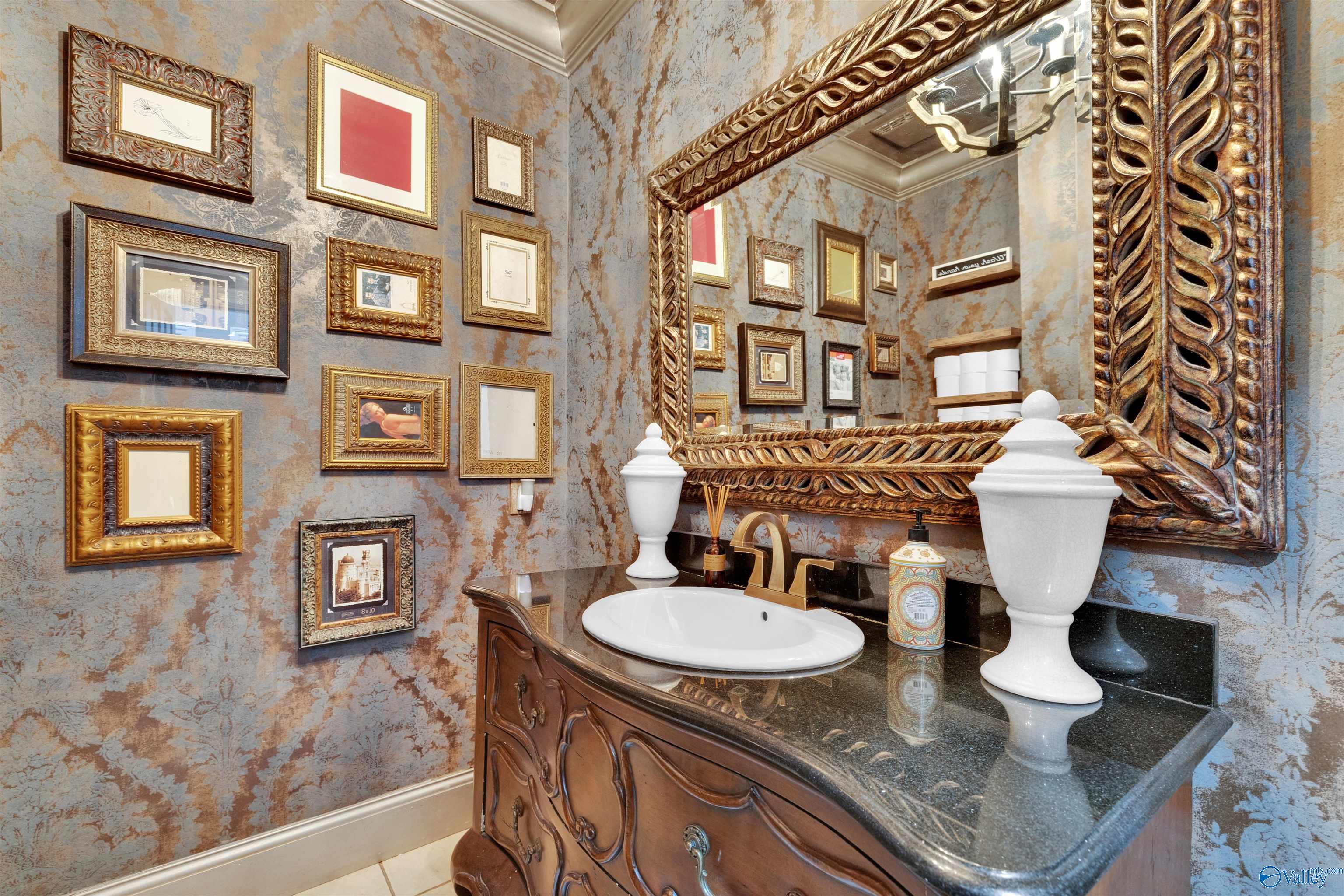 Bathroom with an ornate carved vanity, oversized decorative mirror, and gallery wall of framed pictures.