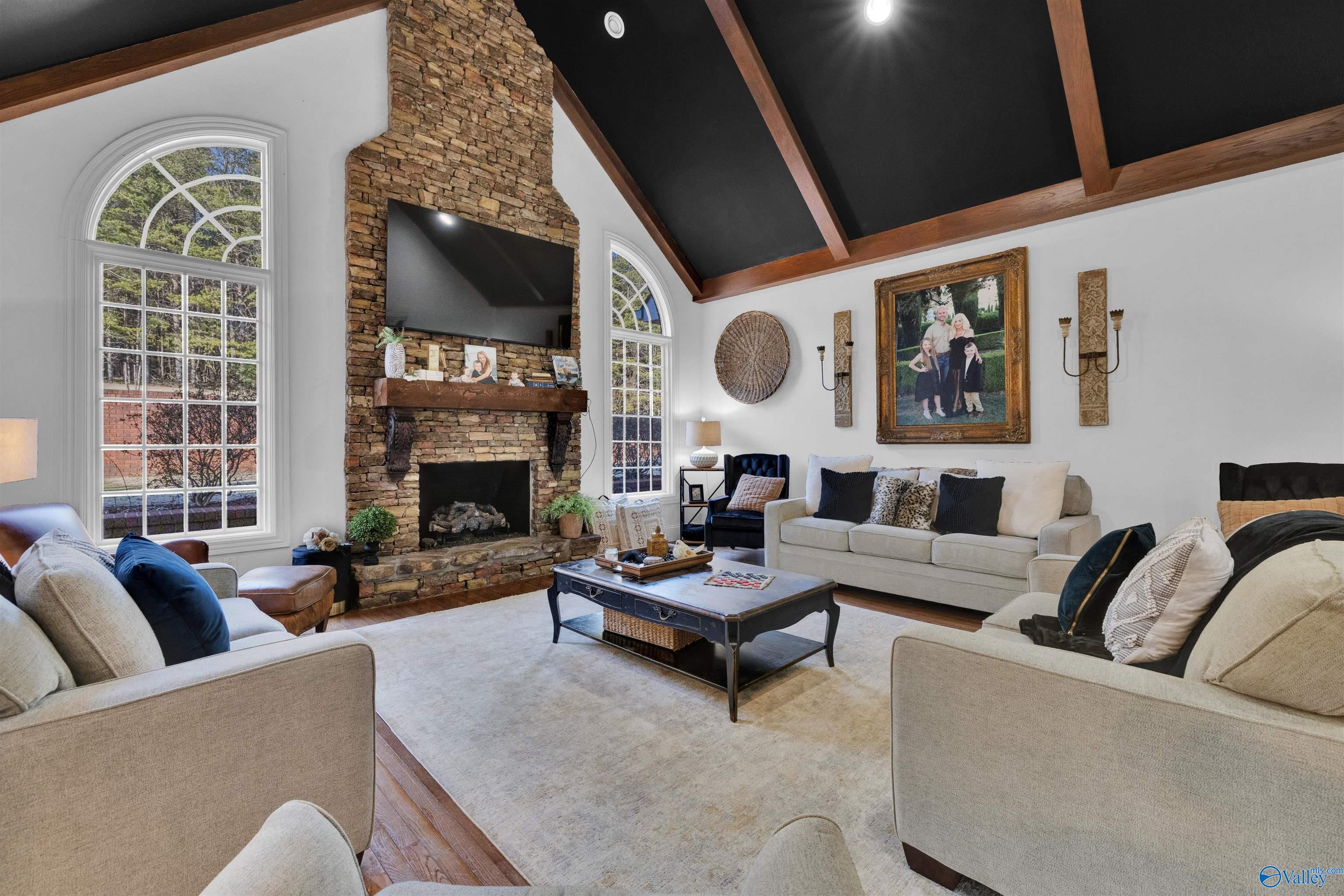 Living room with a vaulted beam ceiling, stone fireplace, arched windows, and neutral seating.
