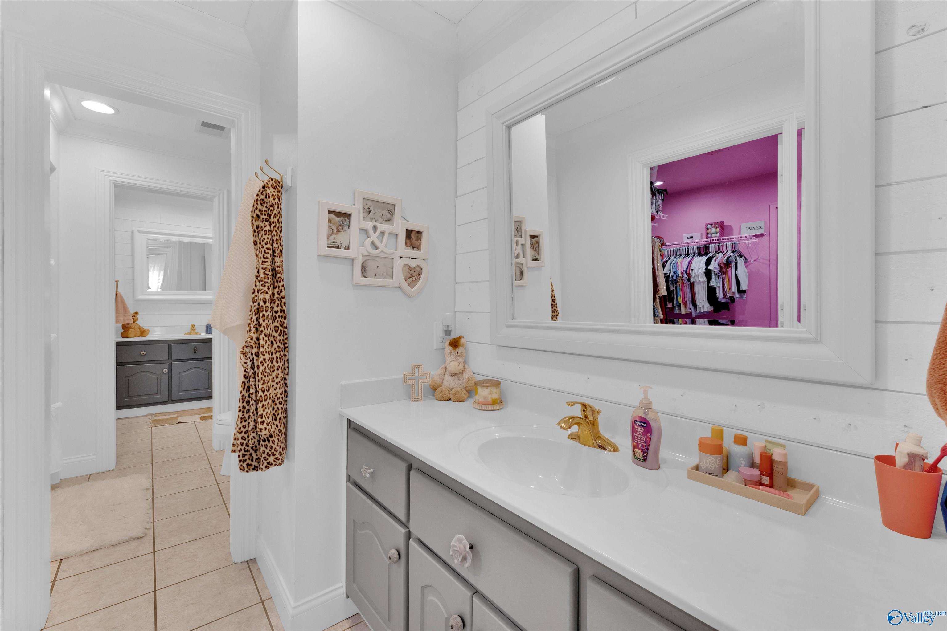 Bathroom vanity with a gold faucet and large mirror reflecting a pink walk-in closet.