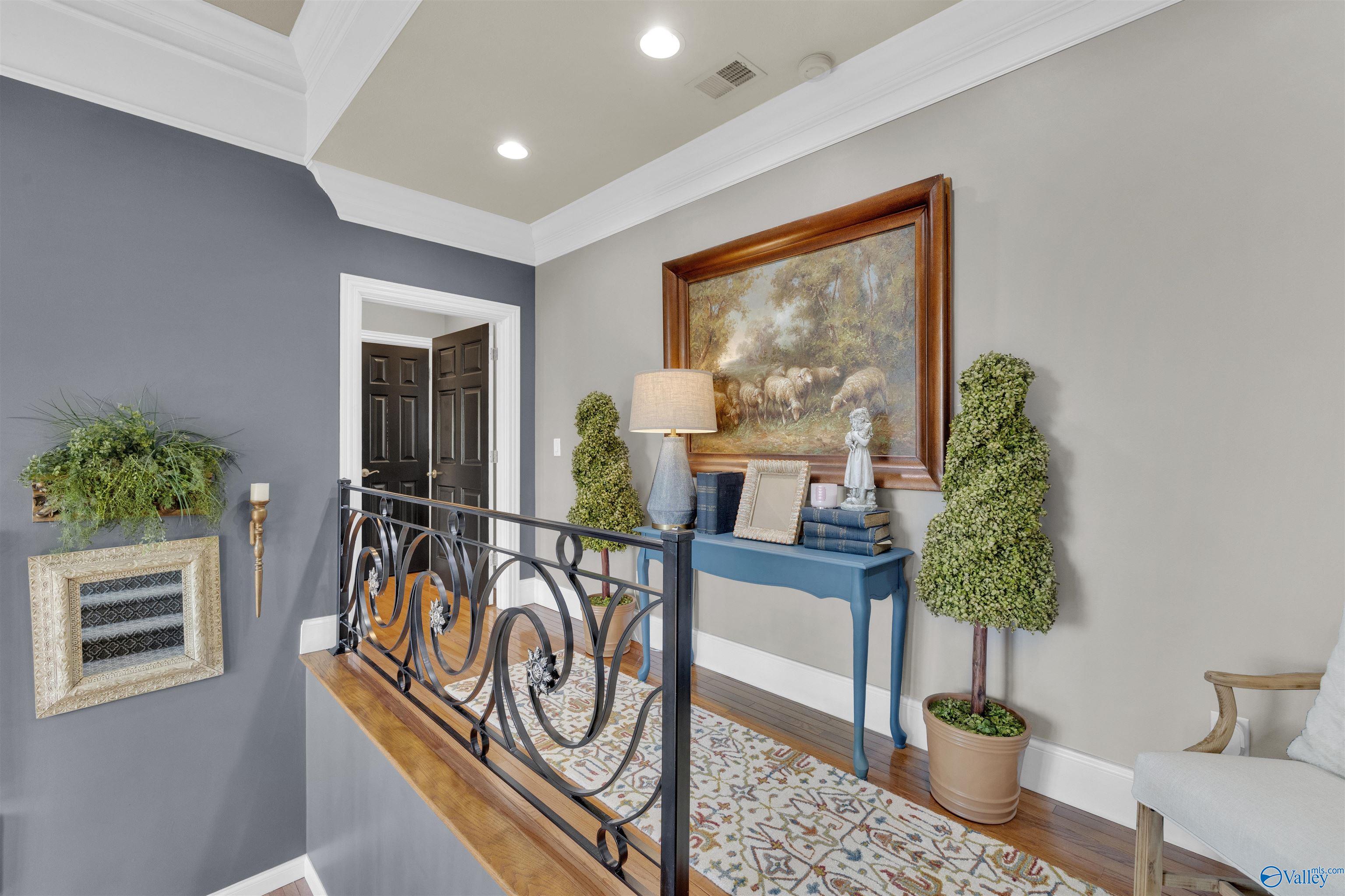Upstairs landing with an ornate iron railing, blue console table, and large framed painting.