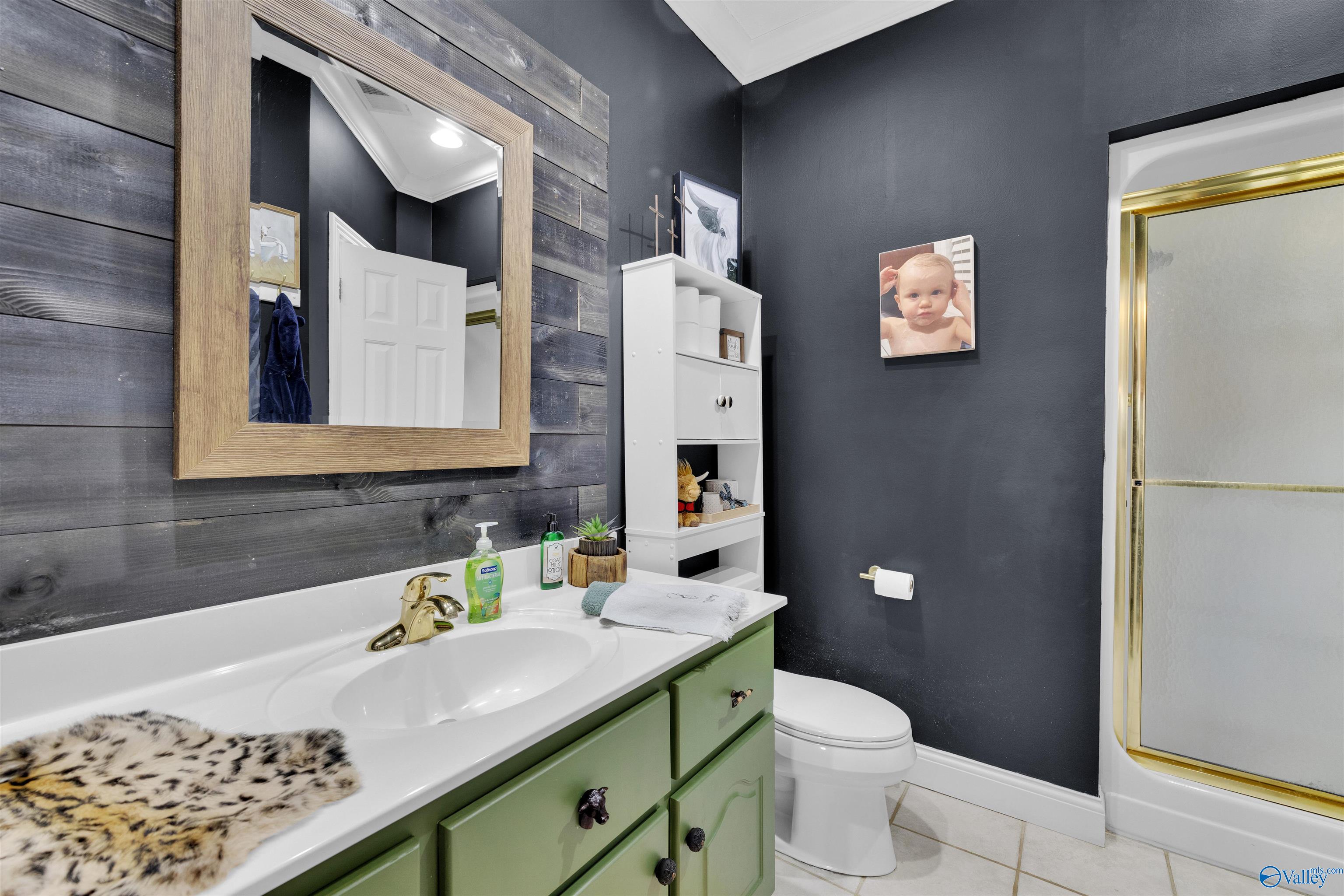 Bathroom with a green vanity, wood-framed mirror, dark walls, and gold-trimmed tub and shower.
