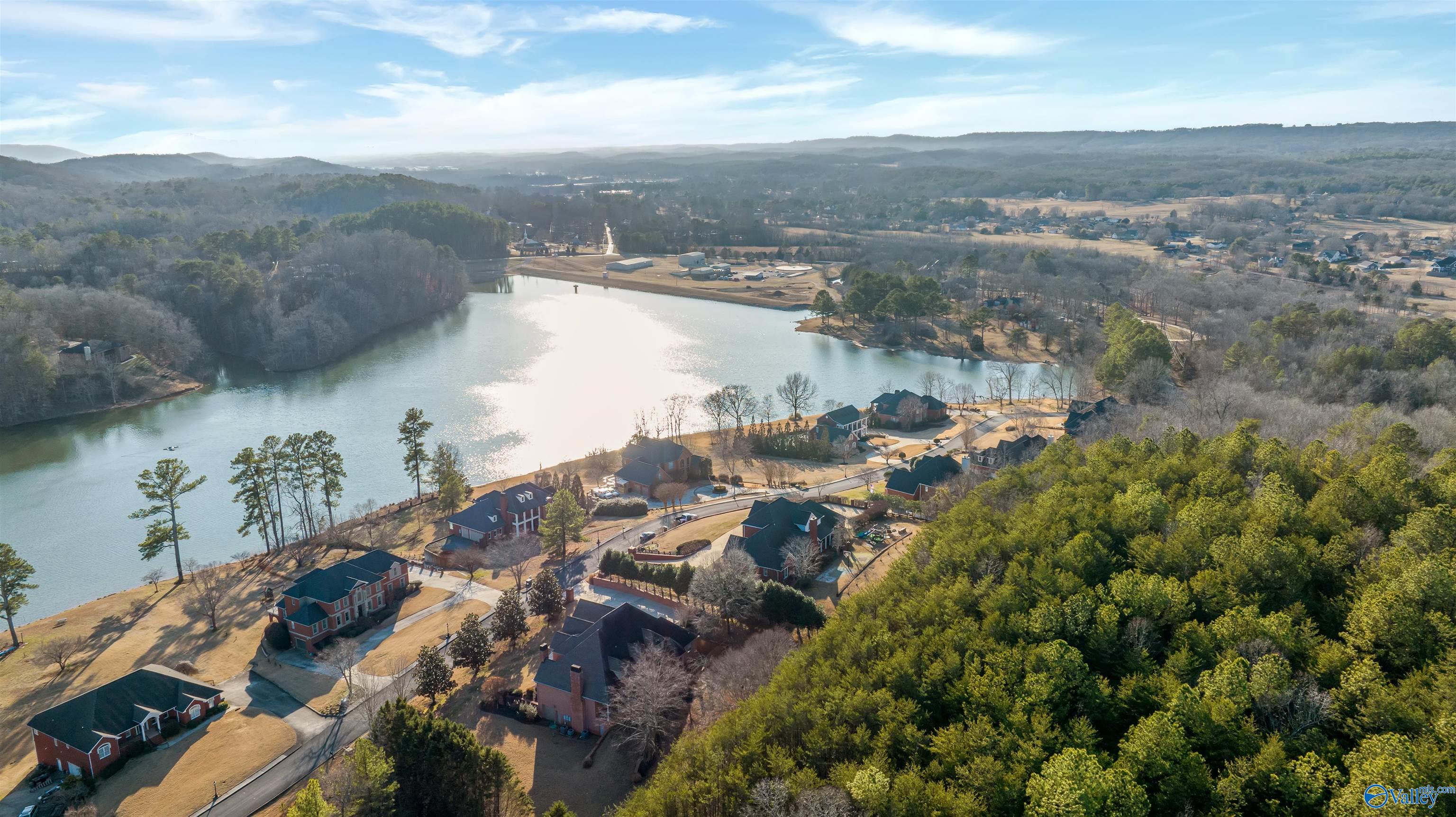 Aerial view of lakeside homes beside a broad lake and wooded hills.