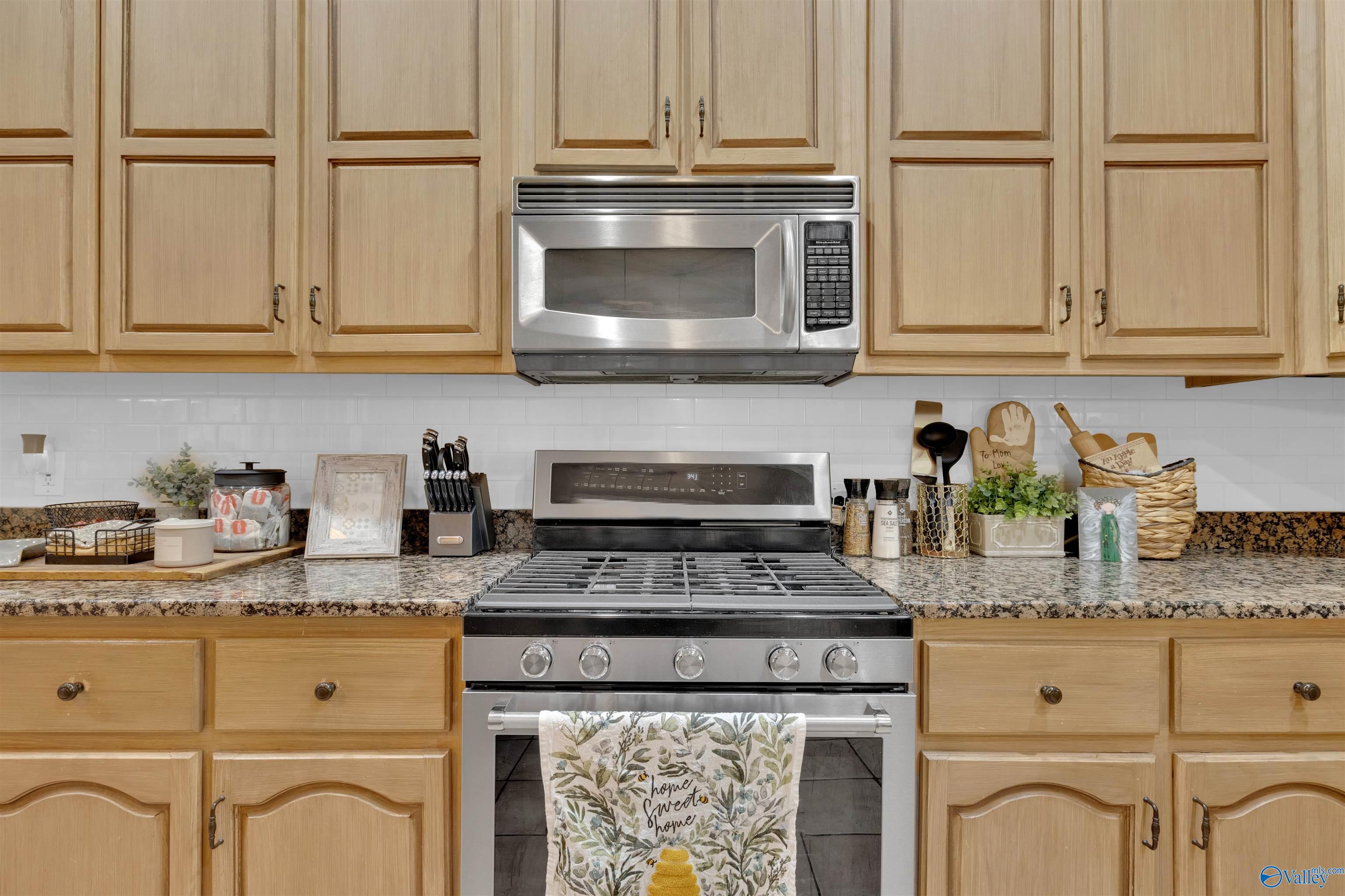 Kitchen with light wood cabinets, granite counters, and a stainless steel gas range and microwave.