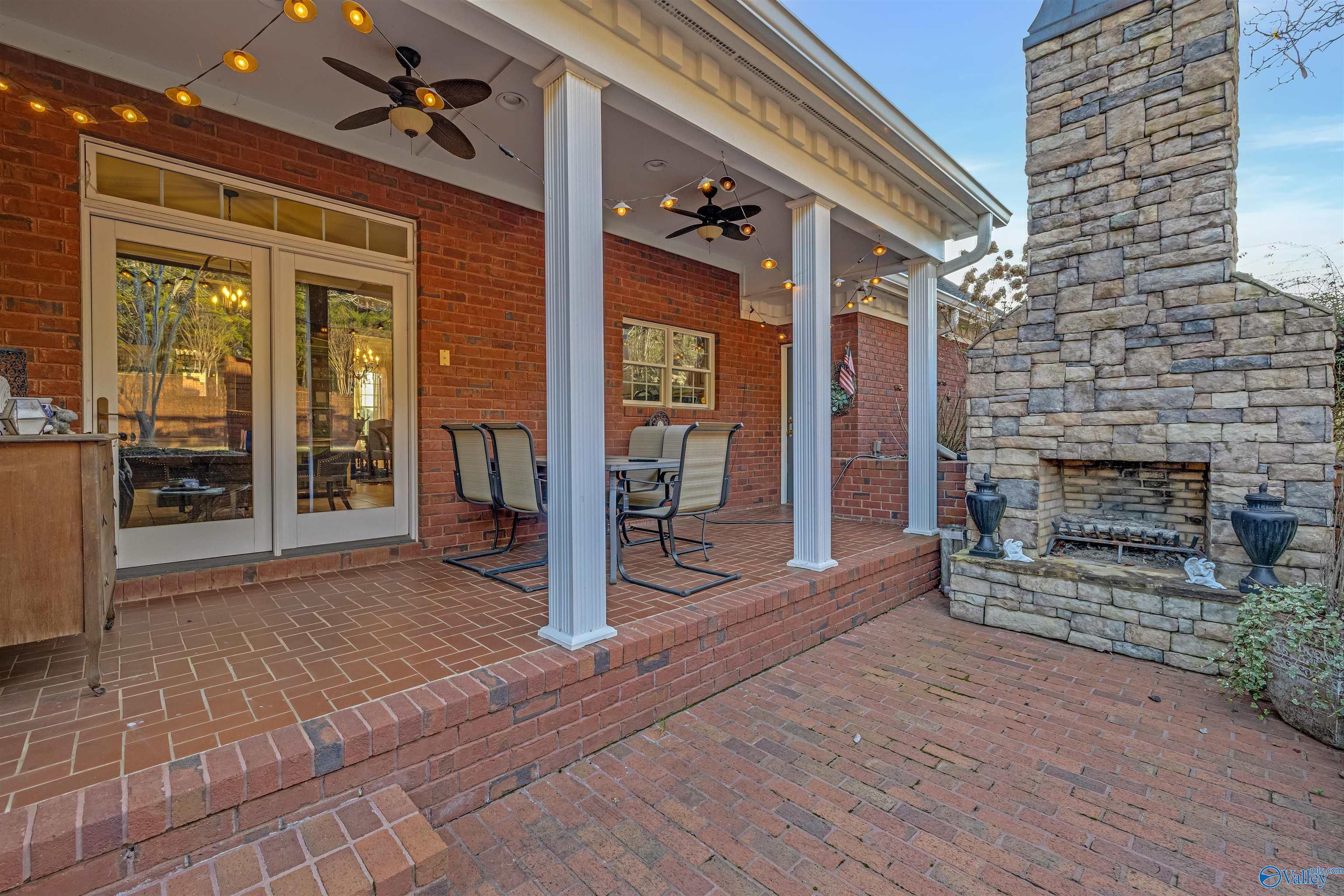 Covered brick patio with white columns, string lights, and a large stone fireplace.