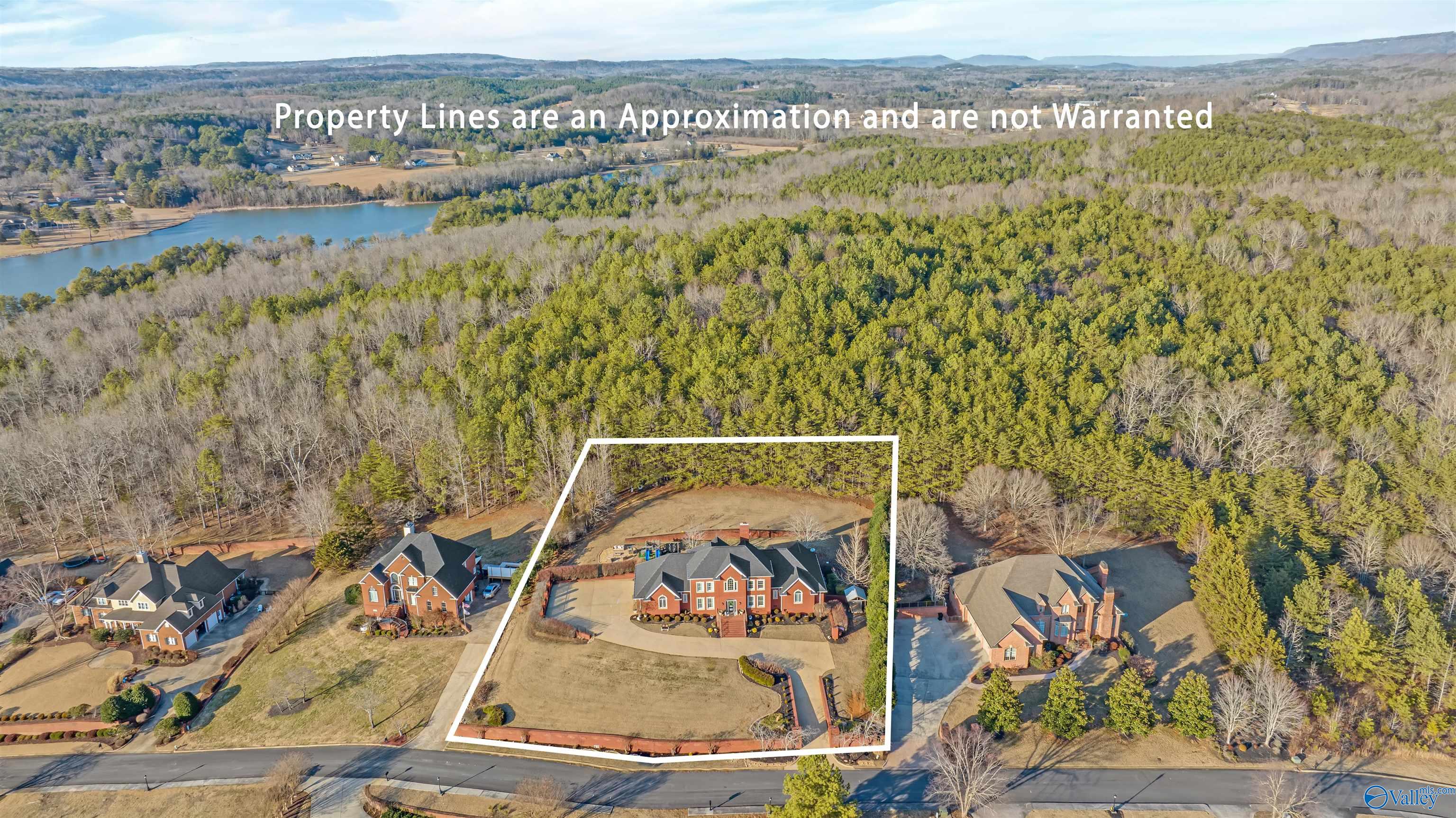 Aerial view of a brick house and lot outlined in white, with woods and a lake beyond.