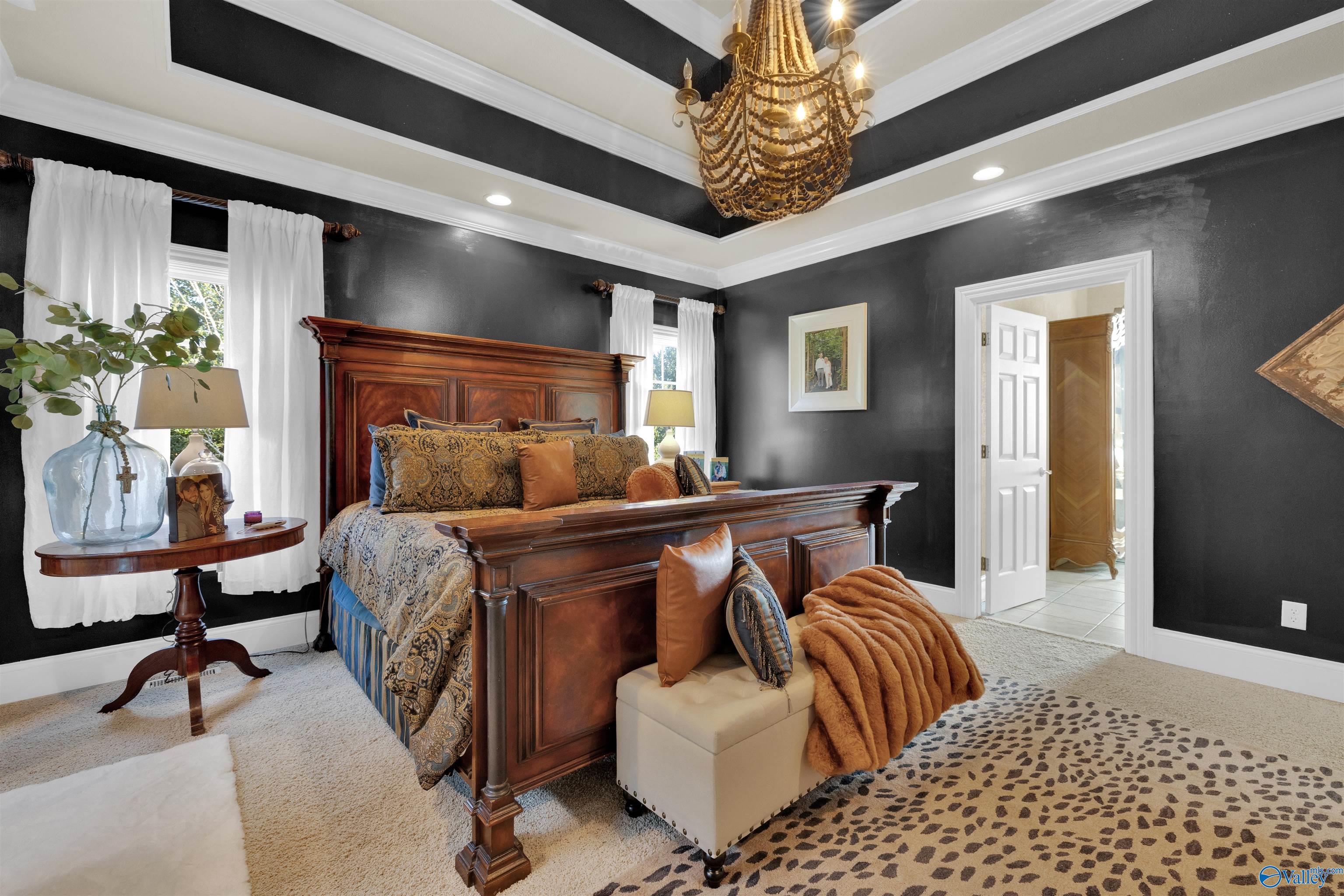 Bedroom with ornate dark wood bed, charcoal walls, beaded chandelier, and animal-print rug.
