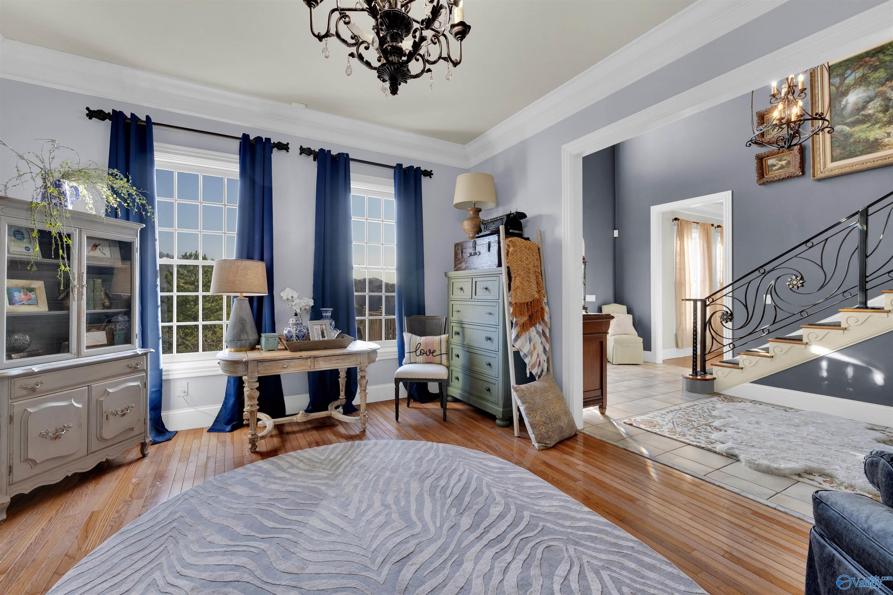 Furnished foyer with tall curtained windows, hardwood floors, and an ornate wrought-iron staircase.
