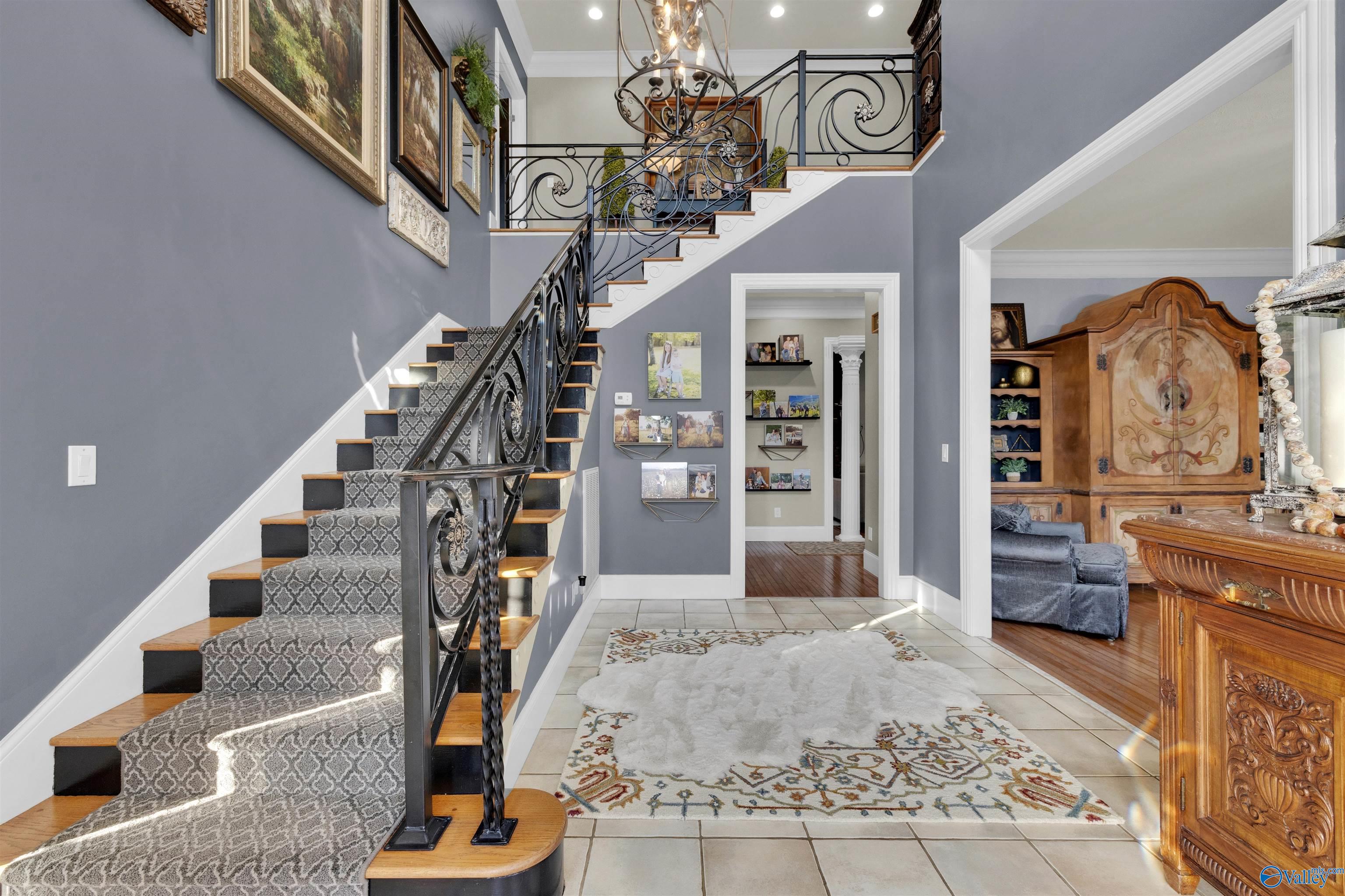 Foyer with a sweeping staircase, ornate iron railings, and a patterned runner.