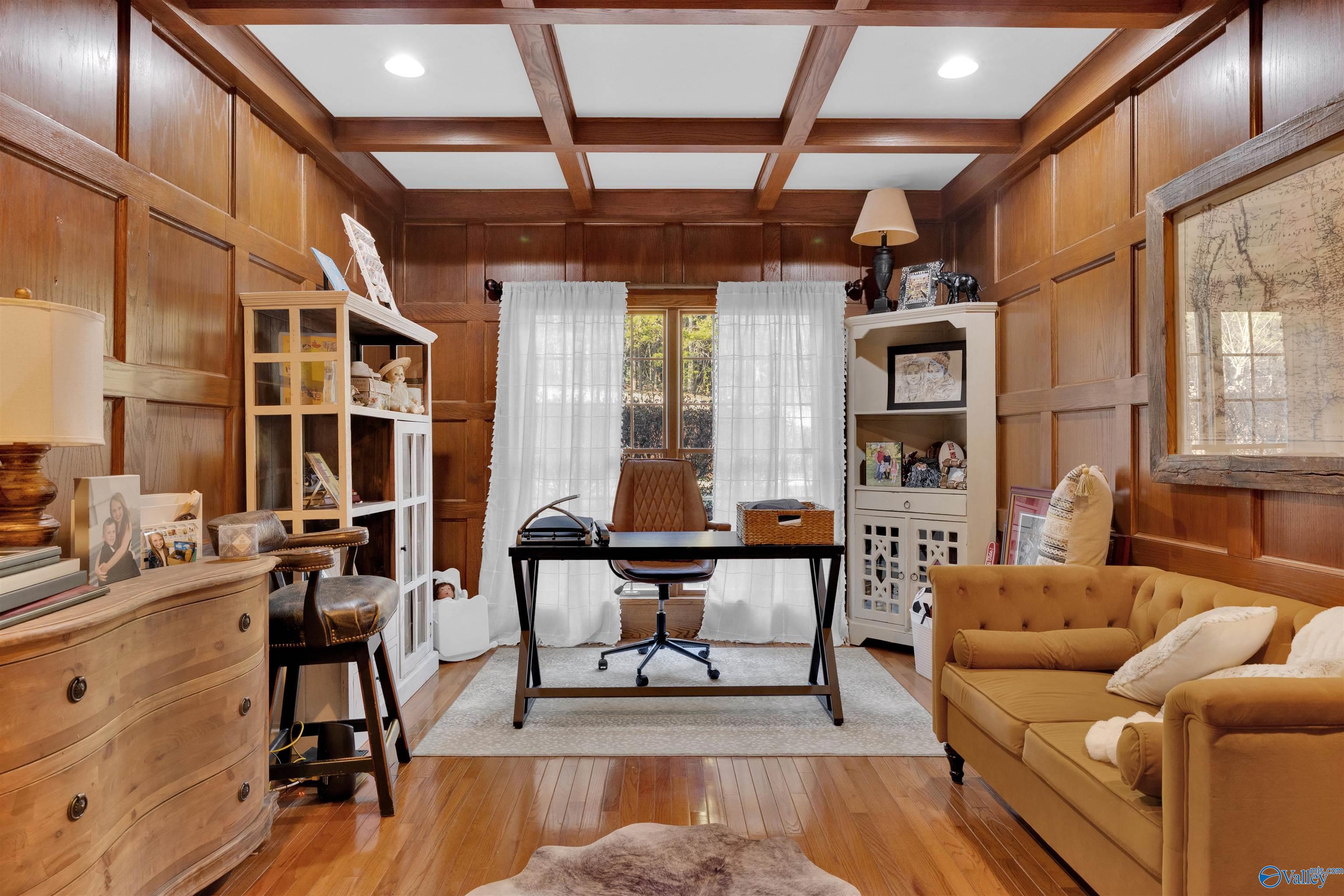 Wood-paneled home office with a central desk, coffered ceiling, built-in shelves, and mustard sofa.