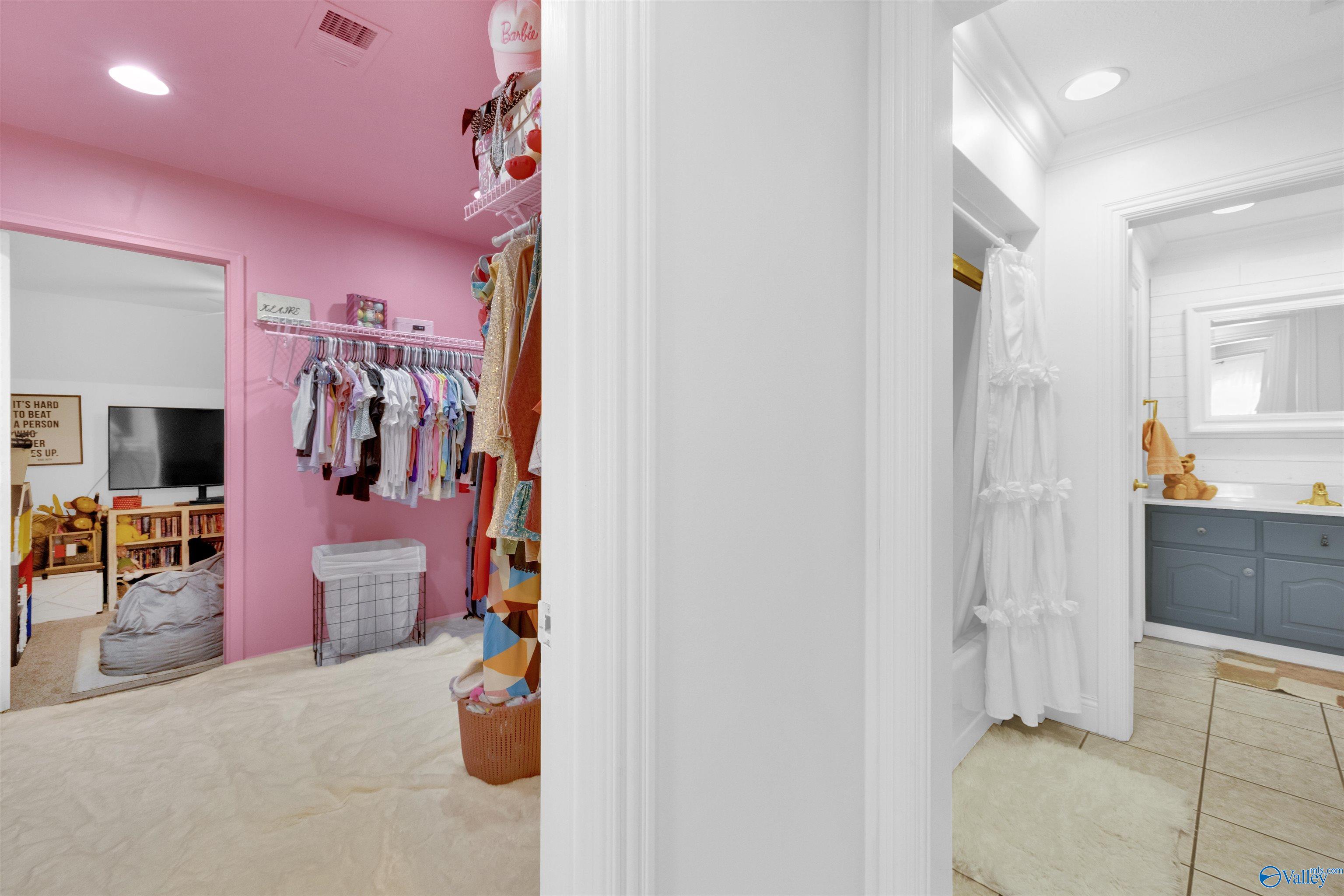 Pink walk-in closet with hanging clothes beside a white bathroom with a blue vanity.