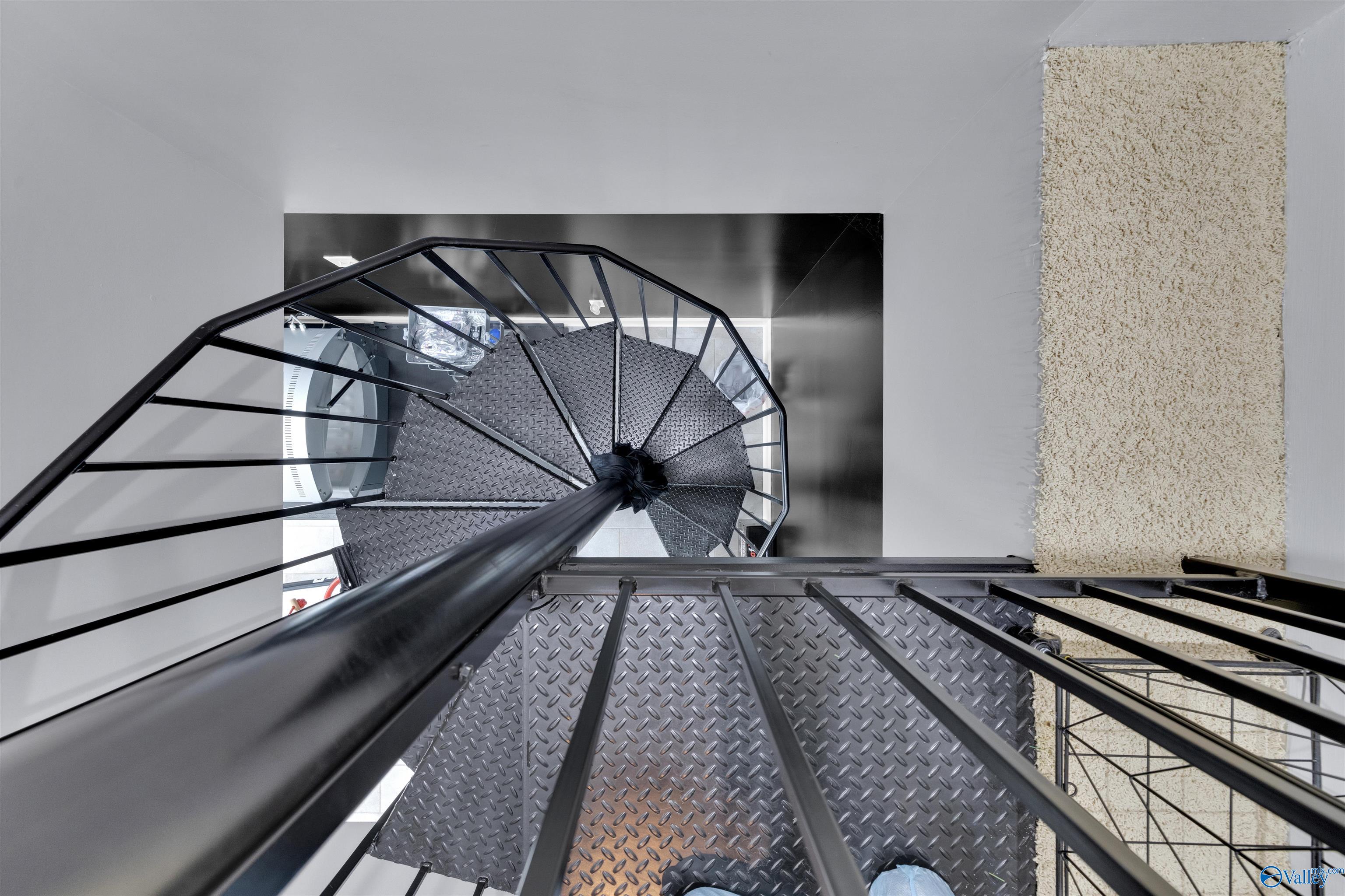 Spiral staircase with dark metal railings and diamond-plate steel treads beside a textured cream wall.