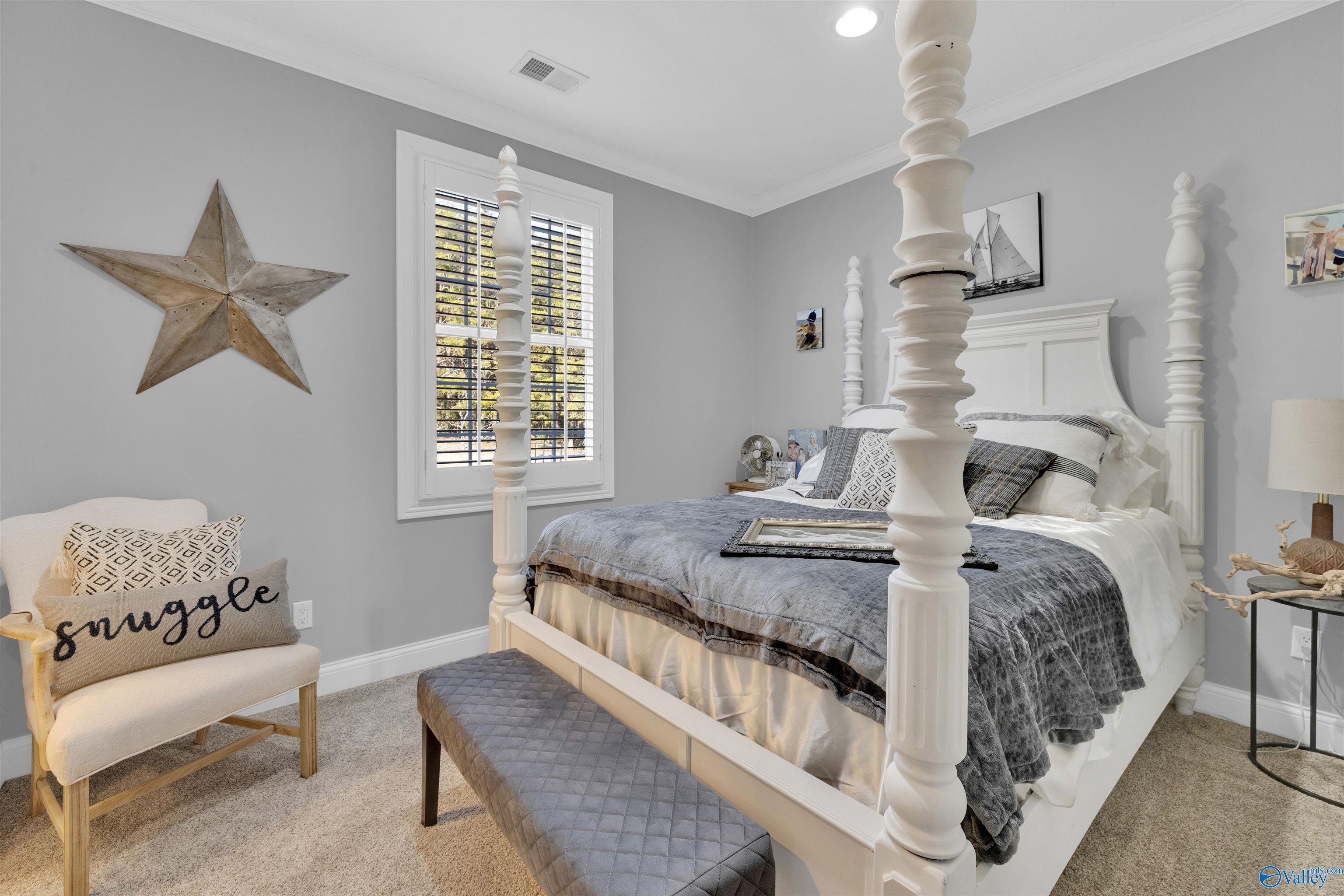 Bedroom with a white four-poster bed, gray bedding, a shuttered window, and a cream chair.