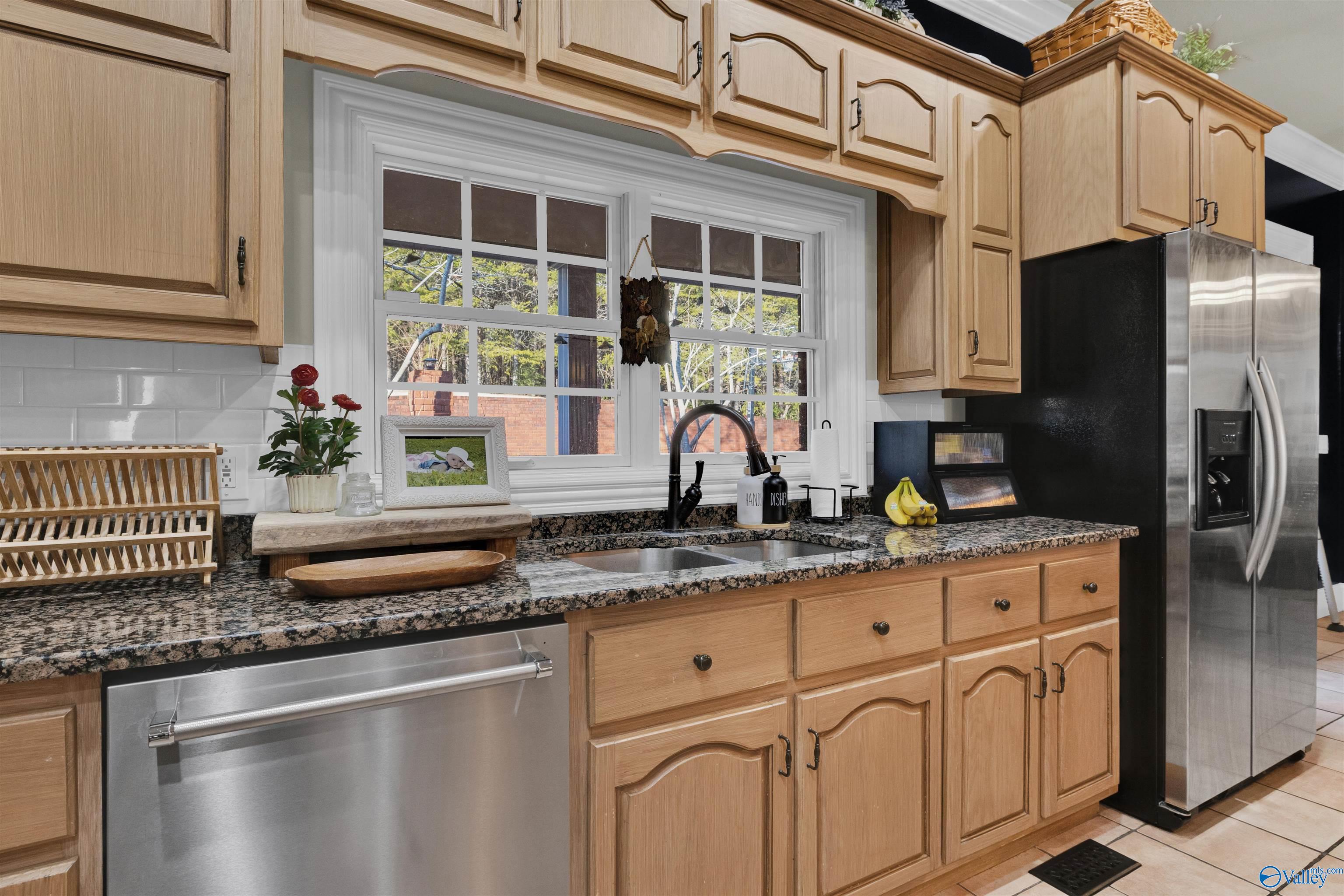 Kitchen with light wood cabinets, granite counters, and a sink beneath two large windows.