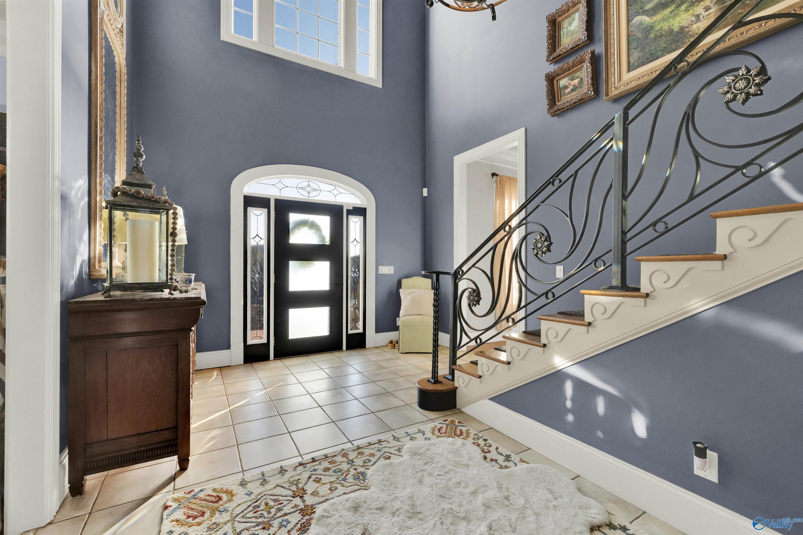 Two-story entry foyer with a glass-paneled door and sweeping staircase with ornate iron railing.