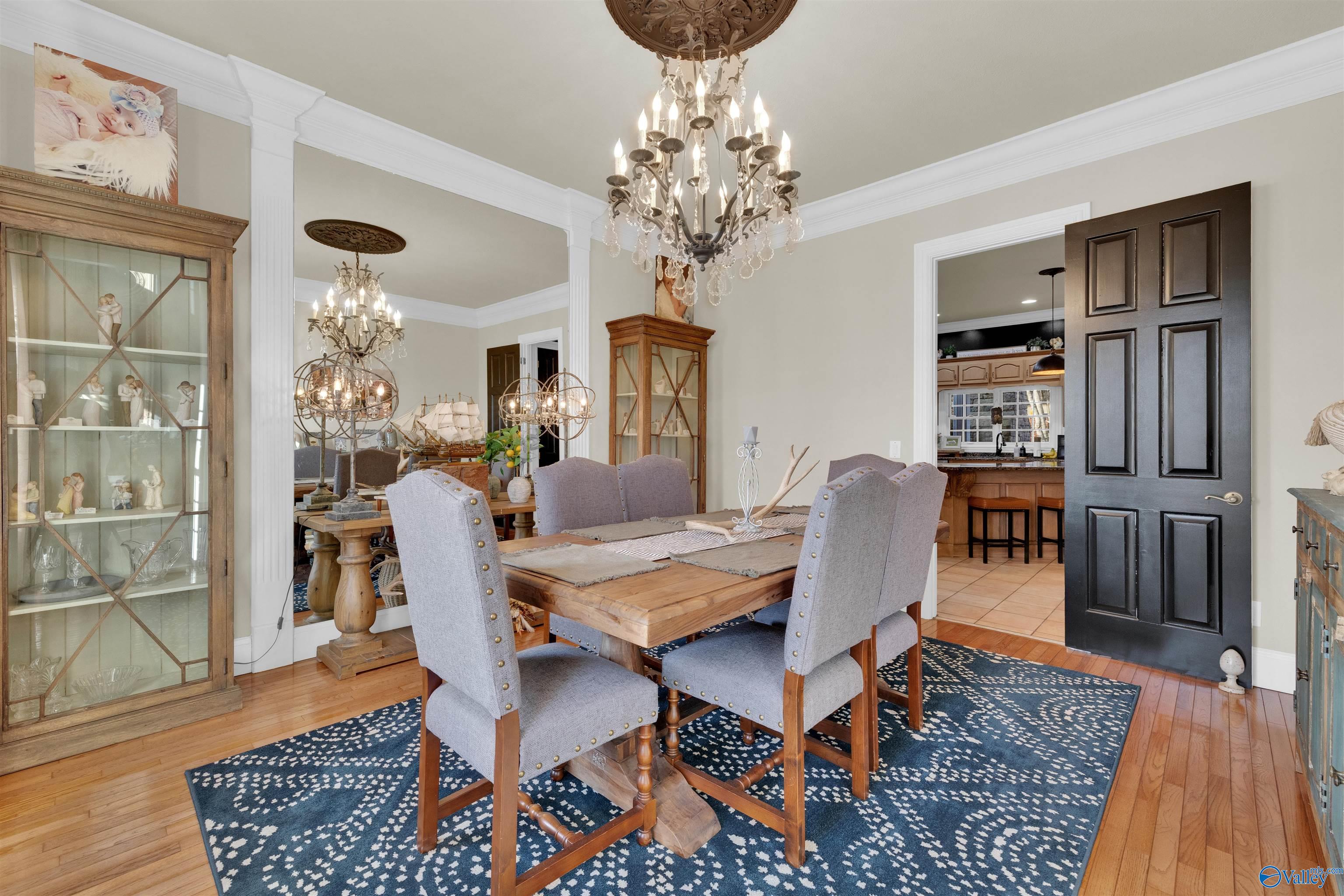 Dining room with a wooden table, gray chairs, ornate chandelier, and blue patterned rug.