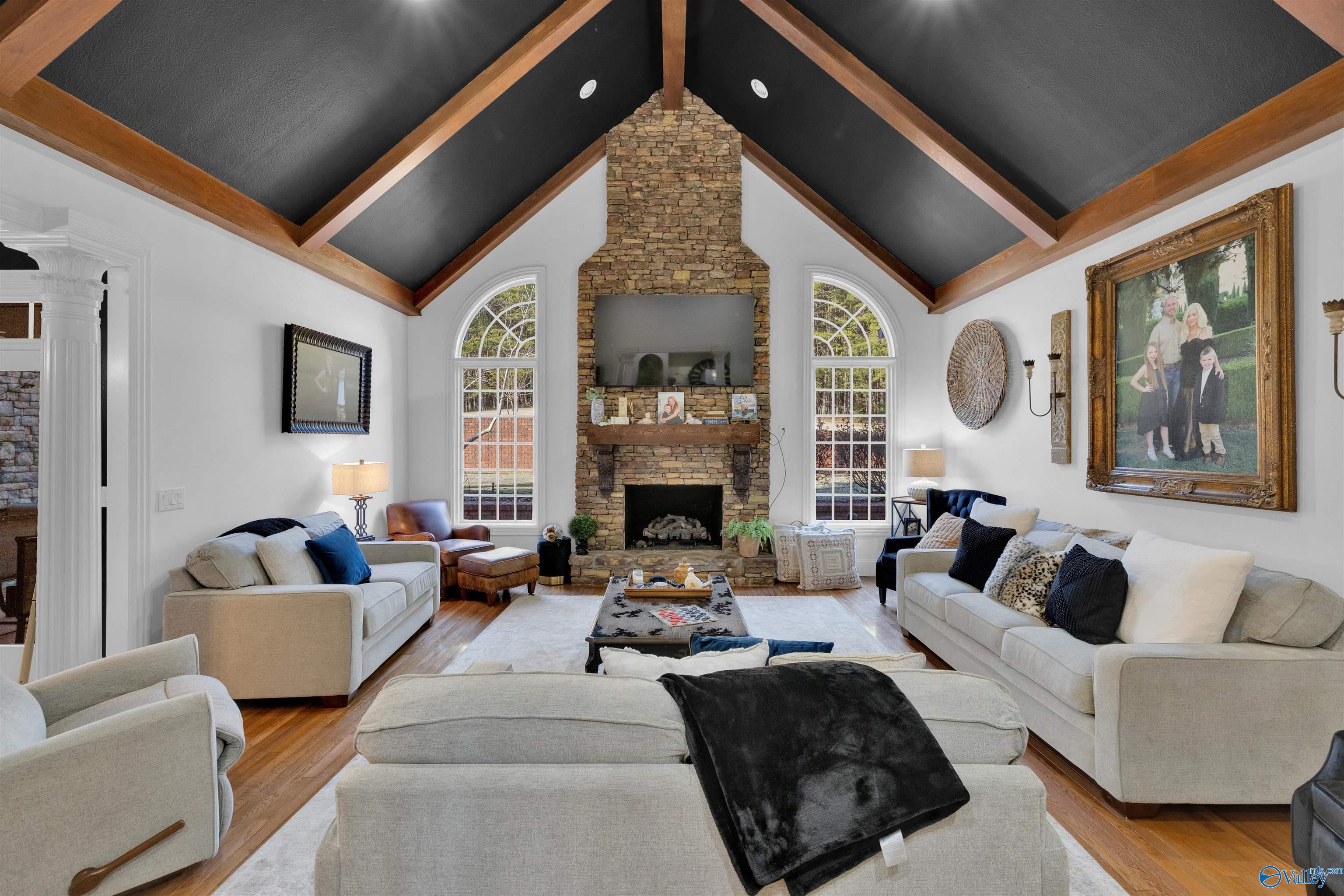 Living room with vaulted beam ceiling, stone fireplace, arched windows, and light sofas.